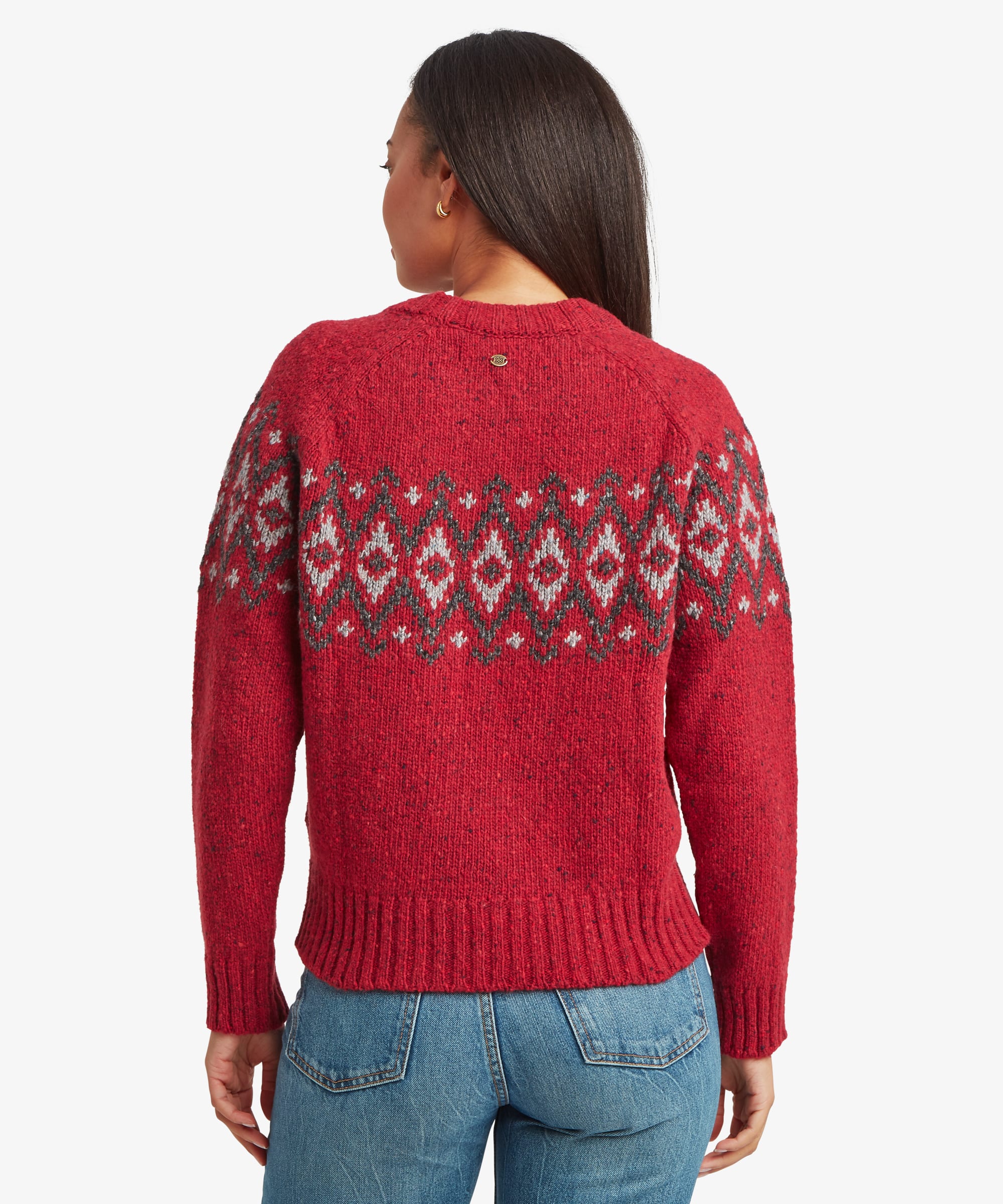 Back view of a woman wearing a red Fair Isle sweater. The upper-back geometric knit pattern and classic crew-neck construction are clearly visible.