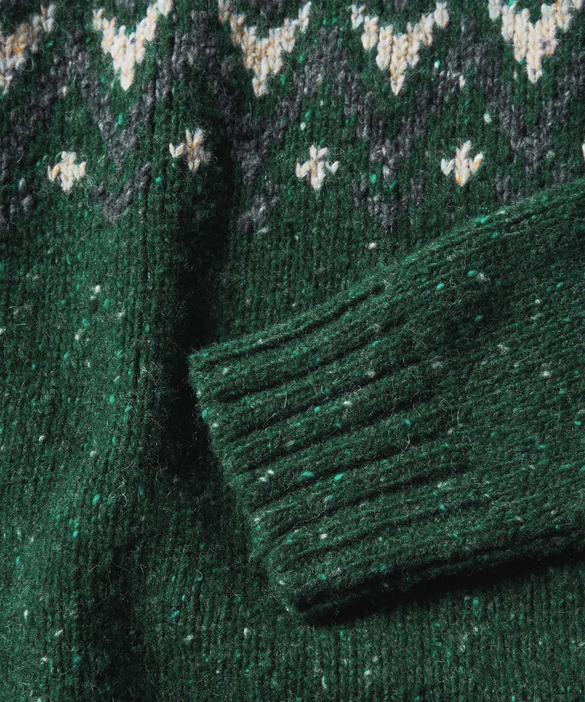Close-up of a dark green knit sweater with a Fair Isle pattern in cream.