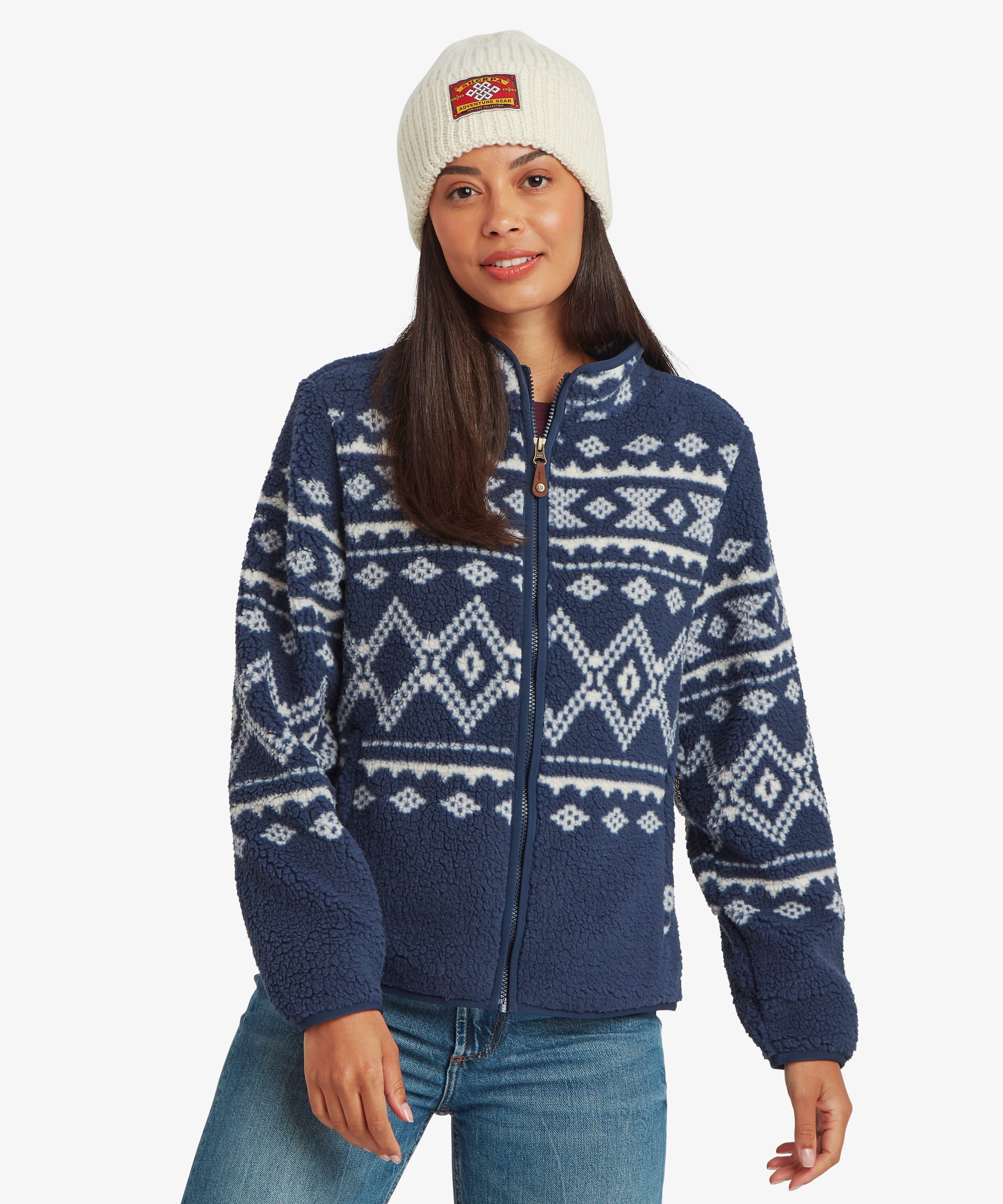 Woman wearing a blue fleece jacket with white Nordic-inspired geometric patterning across the upper body. Front view showing the full-zip closure, stand collar, and cozy textured fleece fabric.