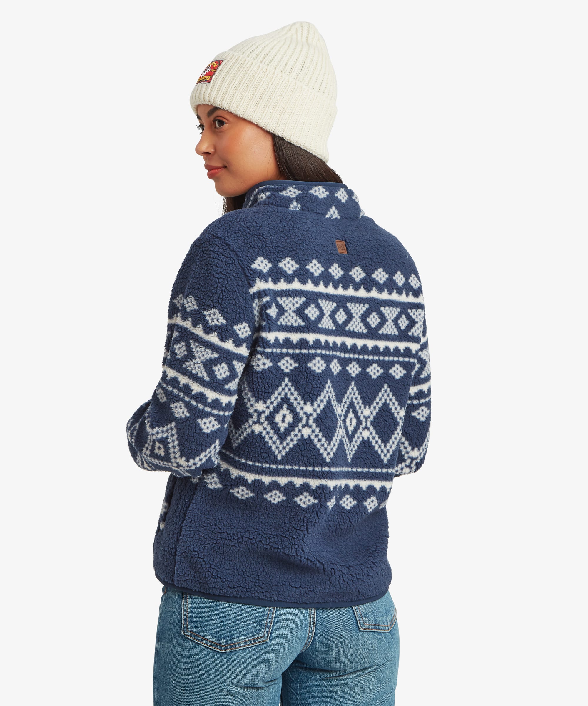 Rear three-quarter view of a woman wearing a blue patterned fleece jacket. The image showcases the wraparound geometric design and soft textured construction.
