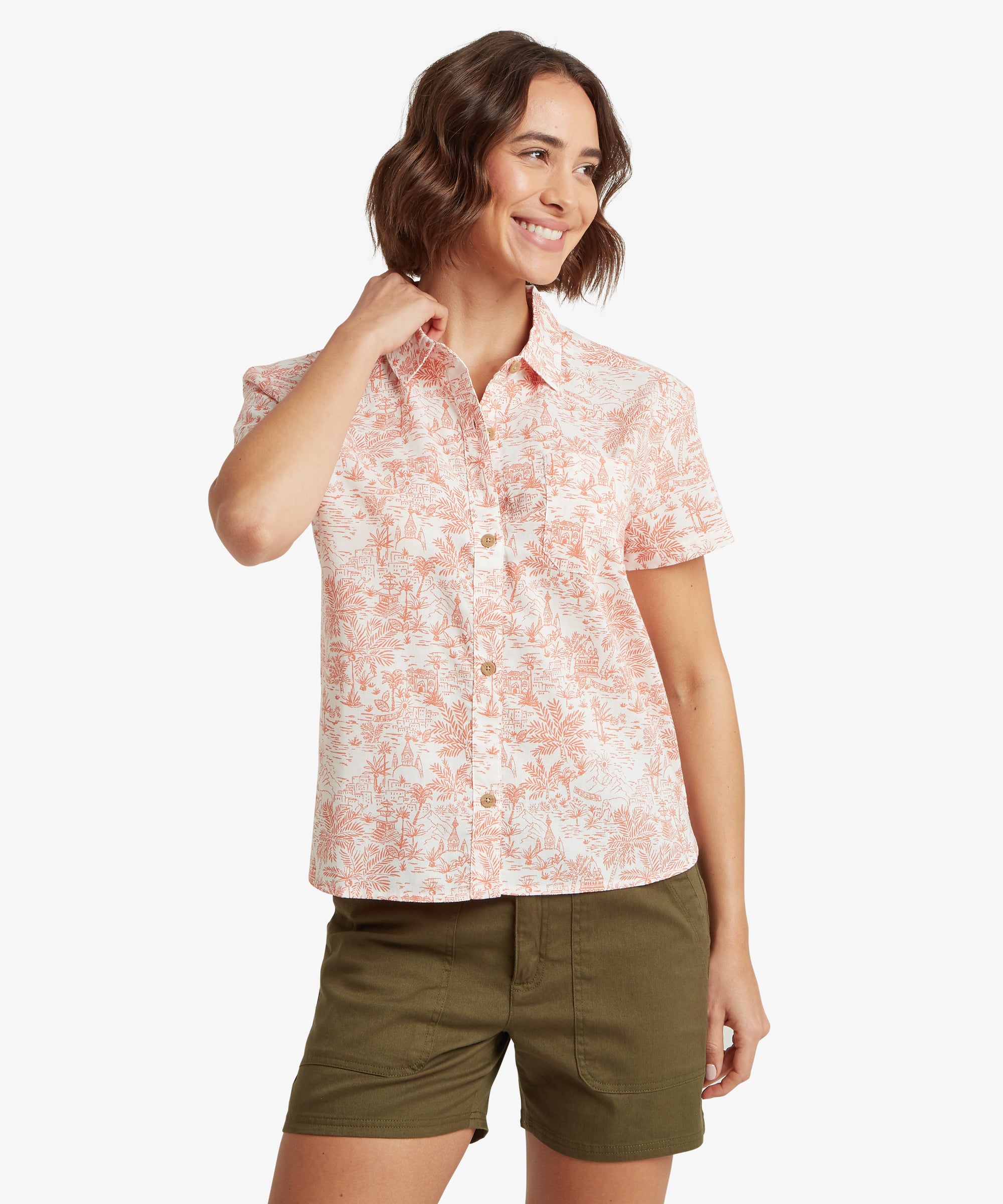 A front-facing view of a woman smiling and wearing the coral toile button-down shirt paired with olive green shorts. The shirt has a comfortable, airy fit through the torso and sleeves, with the hem resting just below the waistline for a relaxed, casual look.