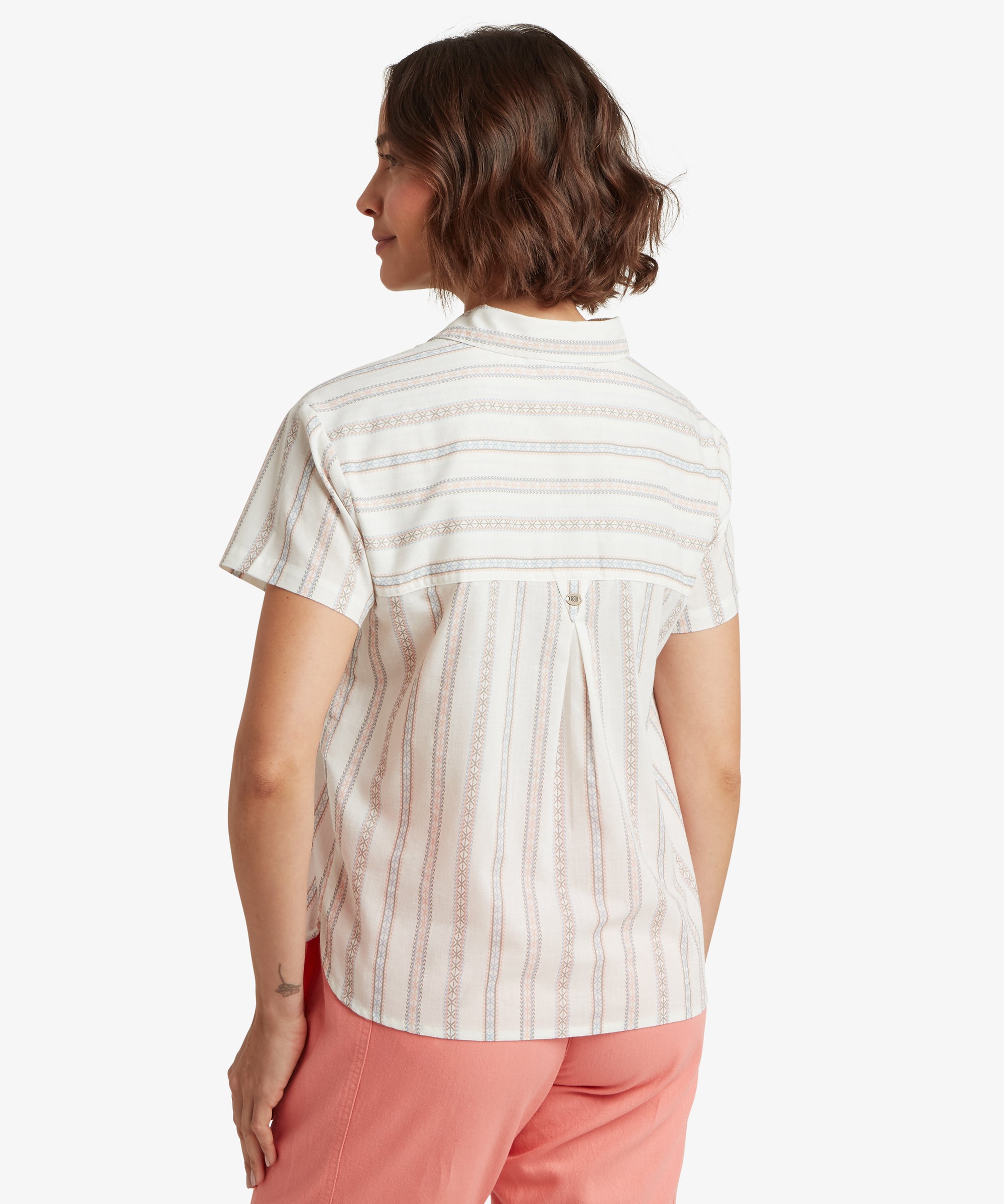 A rear view of the woman showing the back of the striped shirt, which features a horizontal striped yoke and a central box pleat. This design detail adds volume to the relaxed silhouette, allowing the fabric to fall straight and loose over the hips.