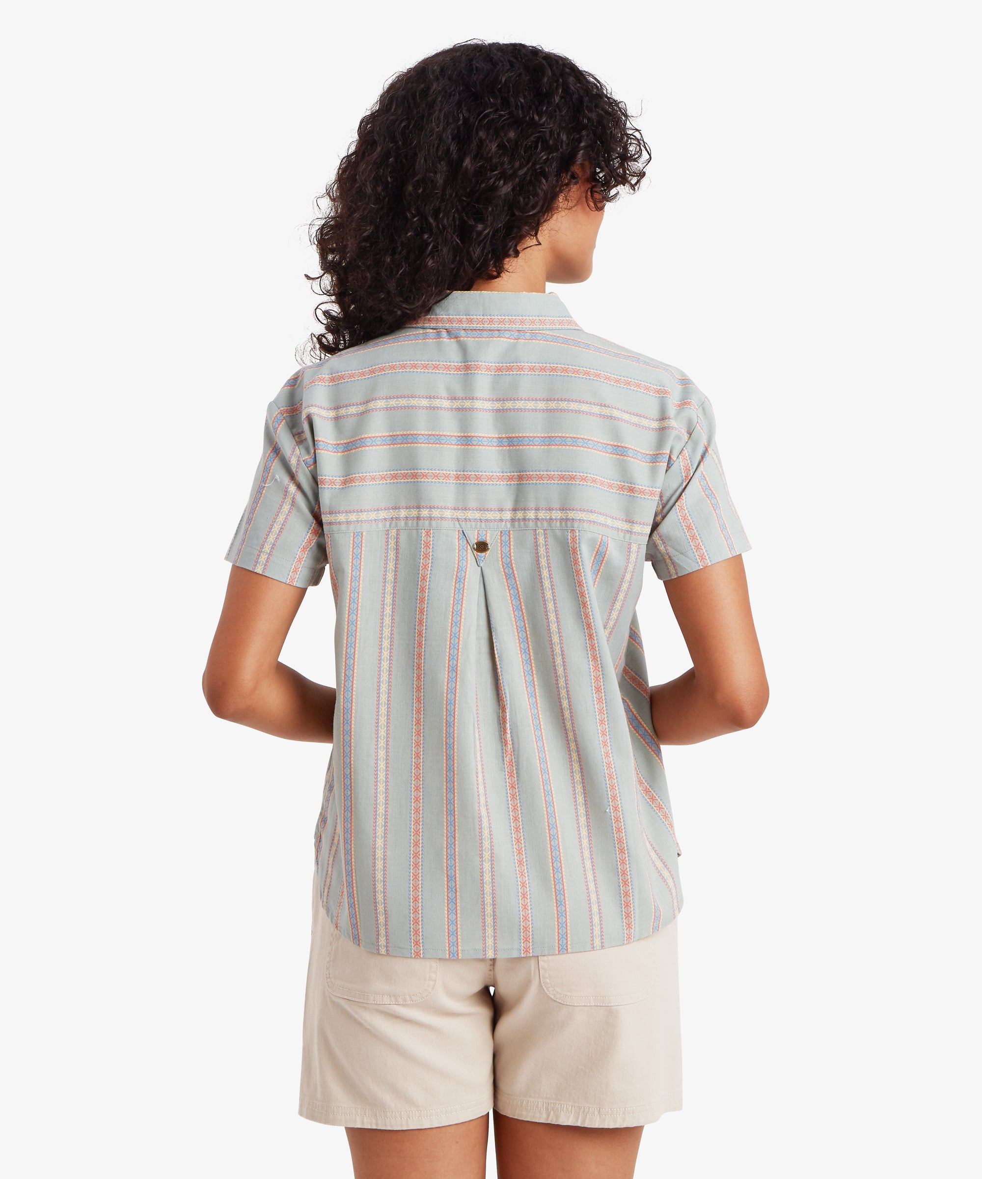 A rear view of a woman wearing the striped button-down, showcasing the functional design details of the back. A horizontal striped yoke sits above a central box pleat, which adds volume and ensures a loose, airy silhouette that moves freely with the body.