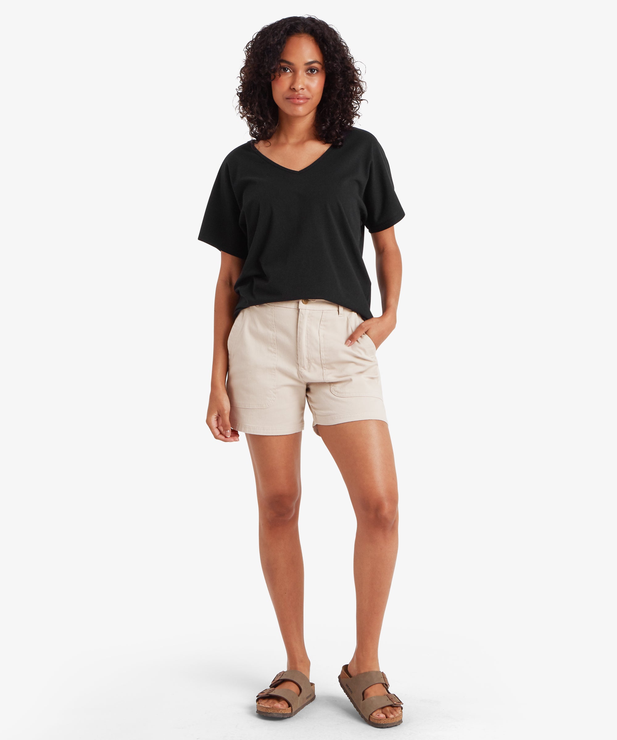 Woman in Jutnu black V-neck T-shirt with beige shorts and brown sandals