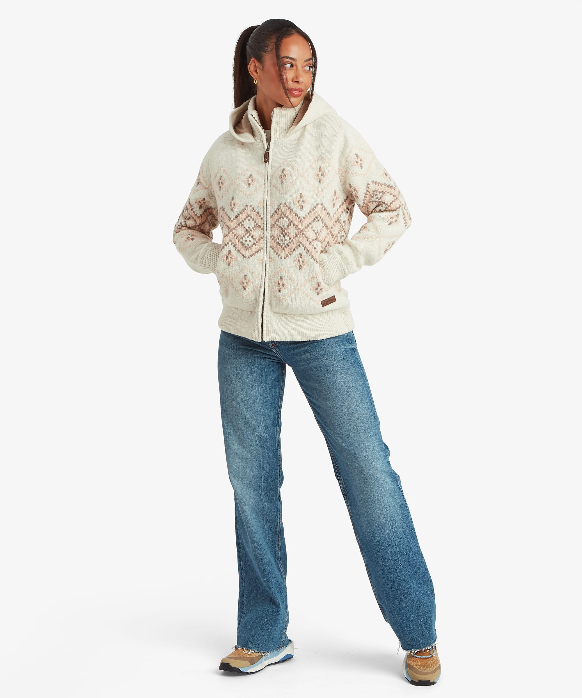 Full-length front view of the women's Kirtipur quarter-zip sweater in white. The patterned knit design extends across the upper body and sleeves, styled with blue jeans against a white studio background.