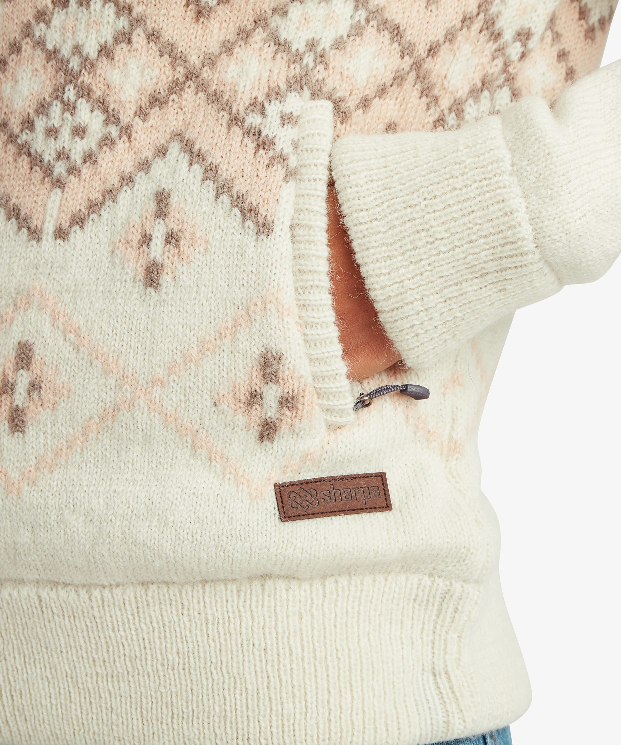 Detailed close-up of the women's Kirtipur sweater in white showing the geometric knit pattern, ribbed hem and signature Sherpa label near the lower side seam.