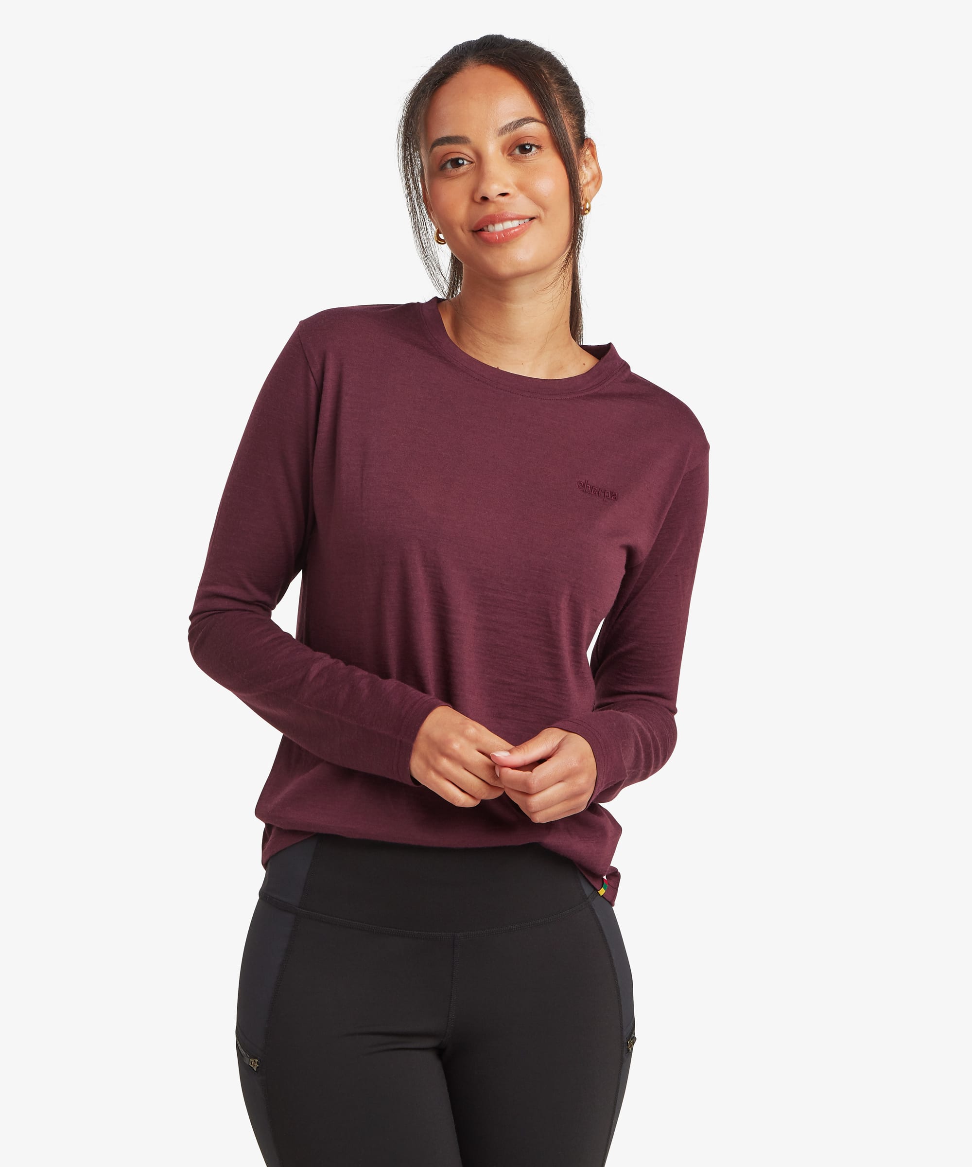 Woman wearing a long-sleeve merino wool T-shirt in a rich burgundy color. Front view showing the lightweight knit fabric, crew neckline, long sleeves, and streamlined athletic fit.