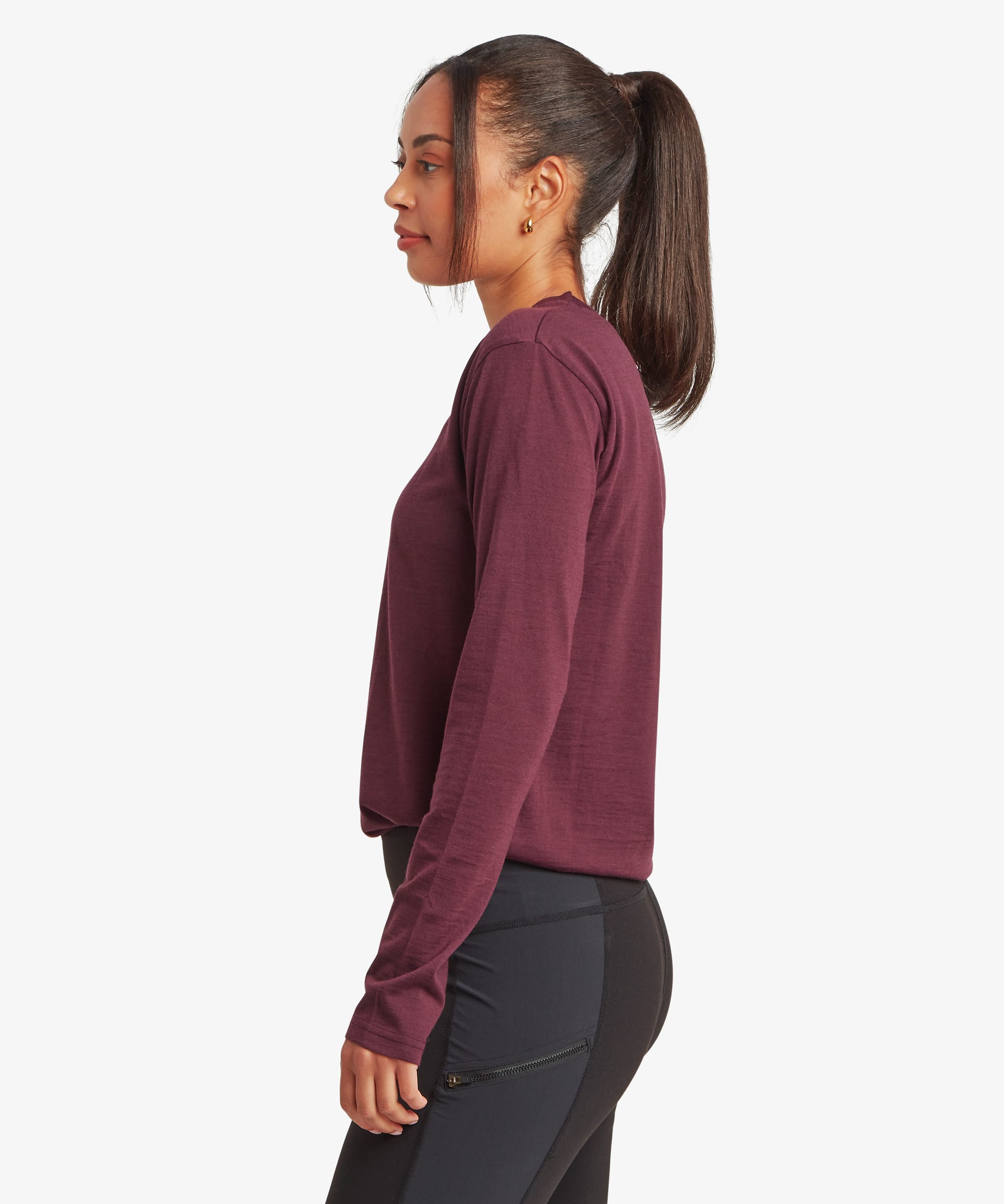 Side-profile view of a woman wearing a burgundy long-sleeve merino T-shirt. The image highlights the smooth fabric, classic crew neckline, and flattering fitted shape.