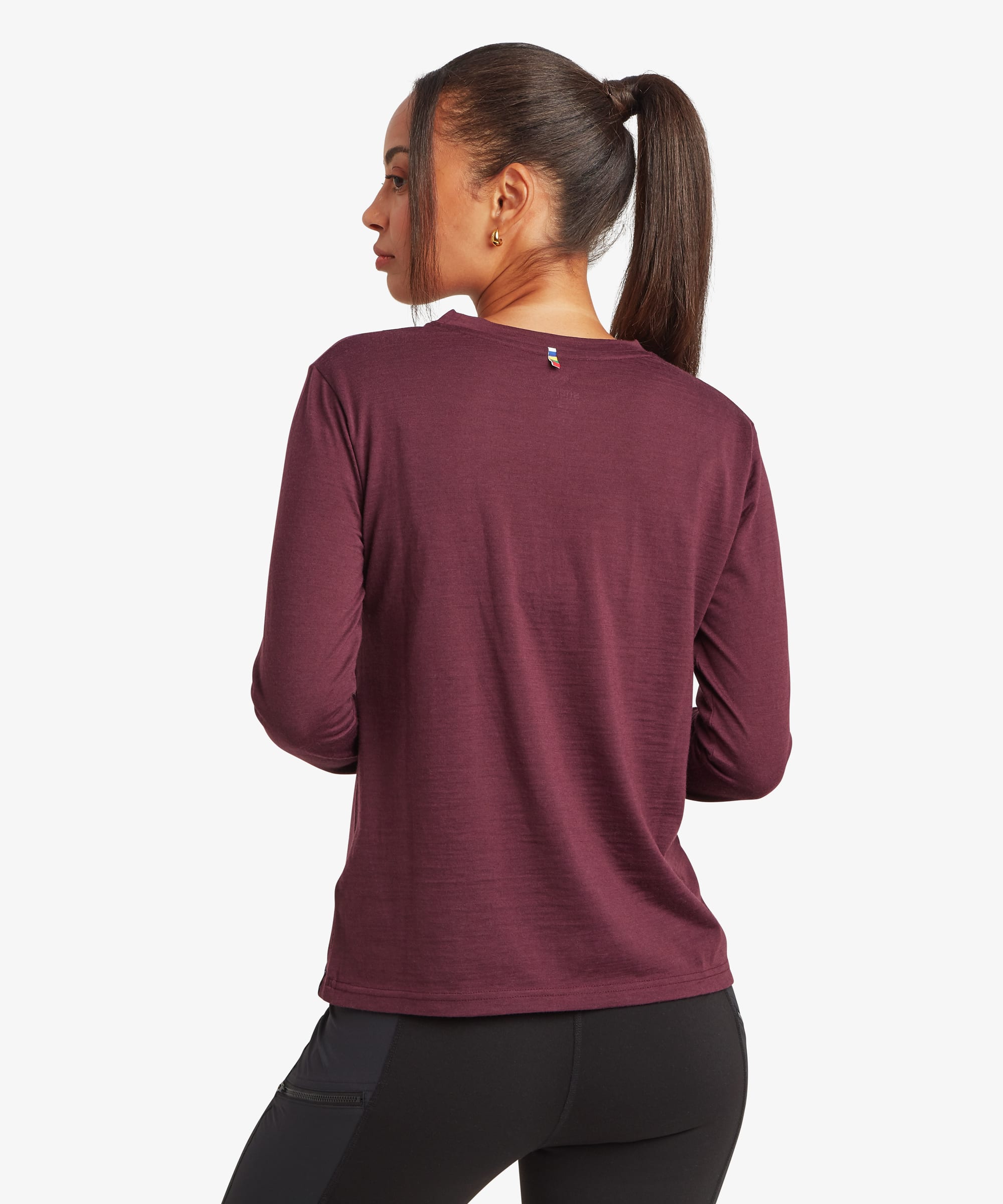 Back view of a woman wearing a burgundy merino wool long-sleeve T-shirt. Features a simple minimalist design, crew neckline, and lightweight fitted construction.