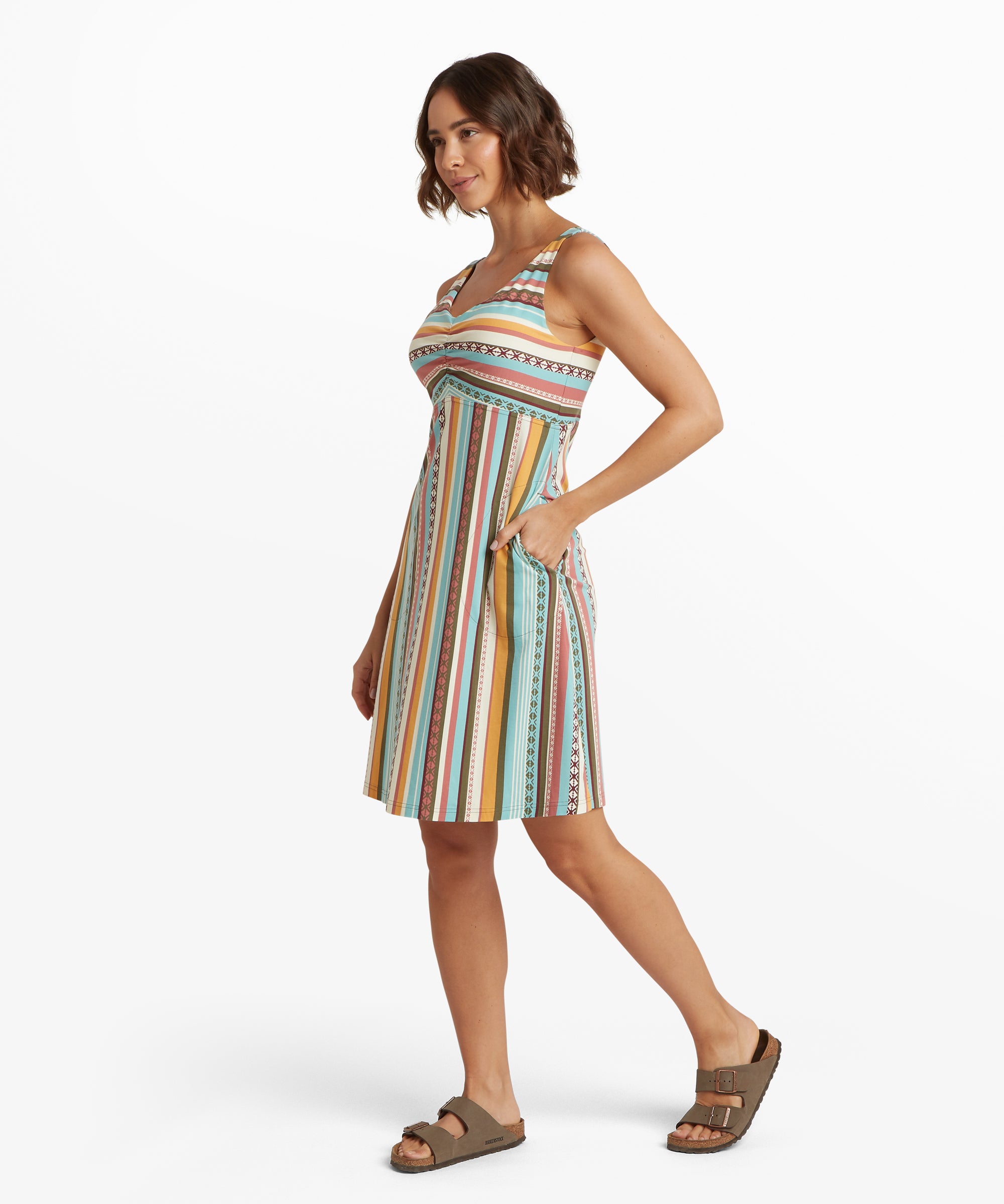 Side view of a sleeveless empire-waist dress with multicolour vertical stripes and decorative geometric bands. A hand rests in the curved side pocket.