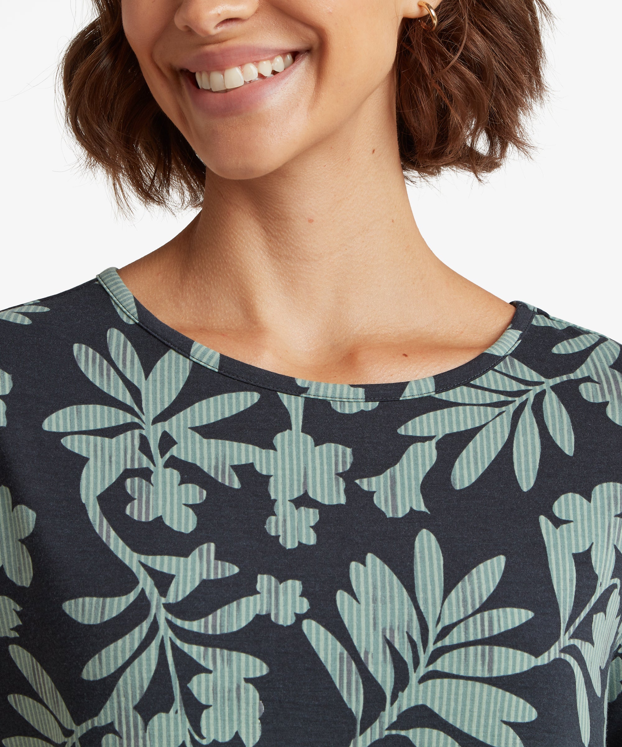 Nahaufnahme des Oberkšrpers mit einem marineblauen T-Shirt, das mit einem sich wiederholenden botanischen Blattmuster in hellen GrŸntšnen verziert ist.