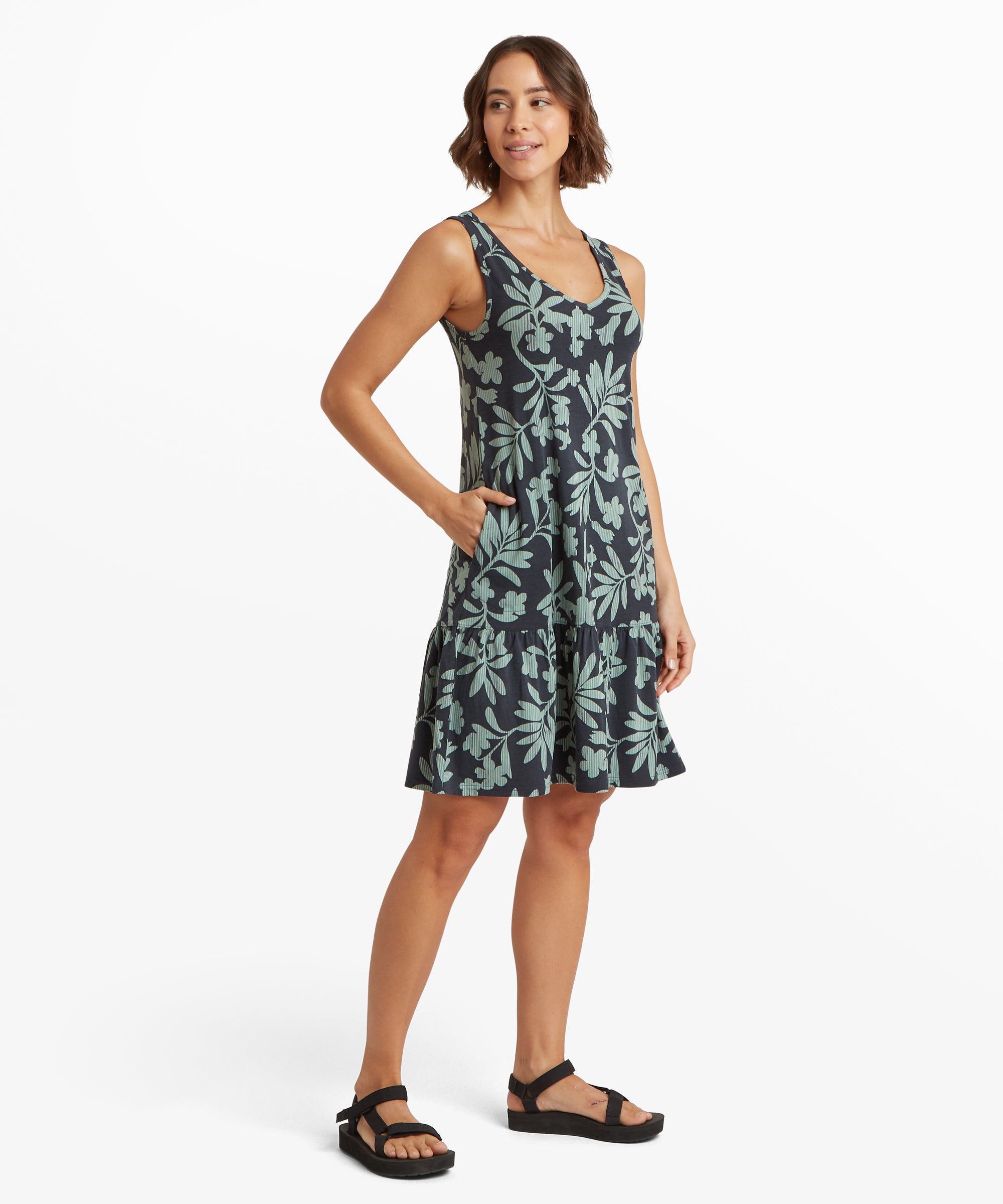 Seitenansicht eines Šrmellosen A-Linien-Kleides mit tŸrkisfarbenem Botanik-Print, gestuftem RŸschen-Saum und einer Hand in der Seitentasche.