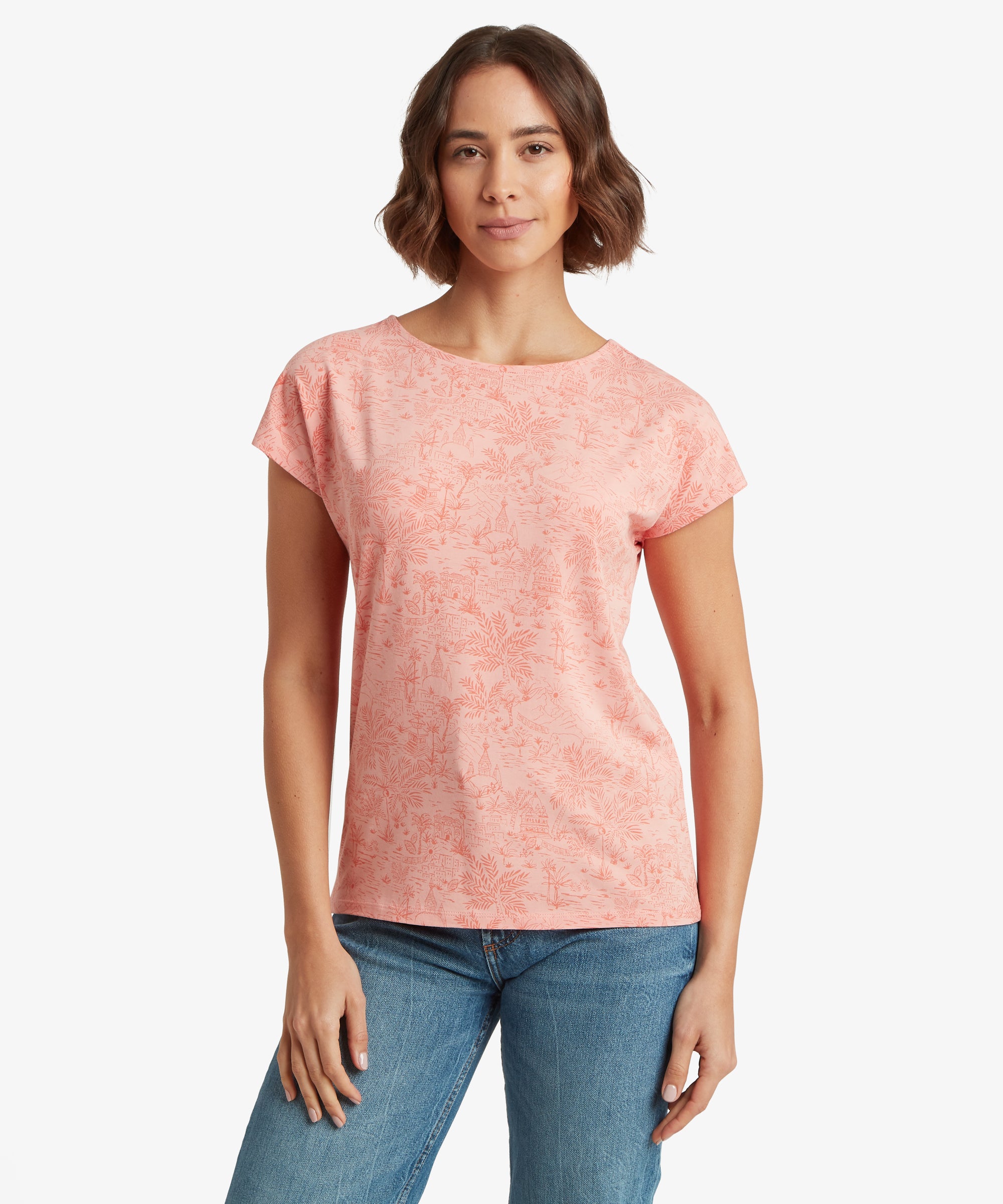 Front view of a light pink scenic Nepalese print T‑shirt styled with blue jeans, showing a relaxed fit and short sleeves.