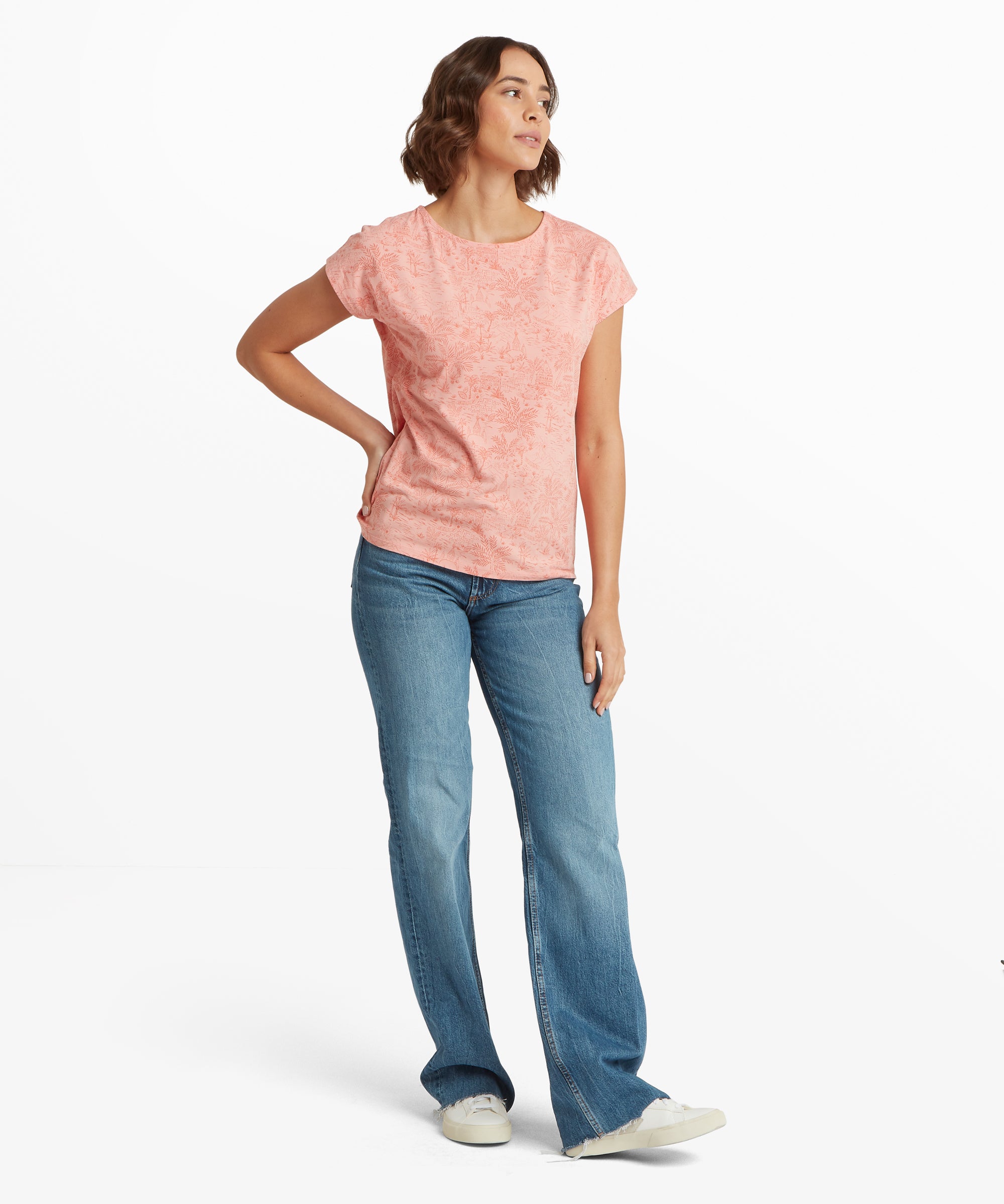 Full‑body view of a soft pink printed T‑shirt paired with blue jeans and white casual trainers.