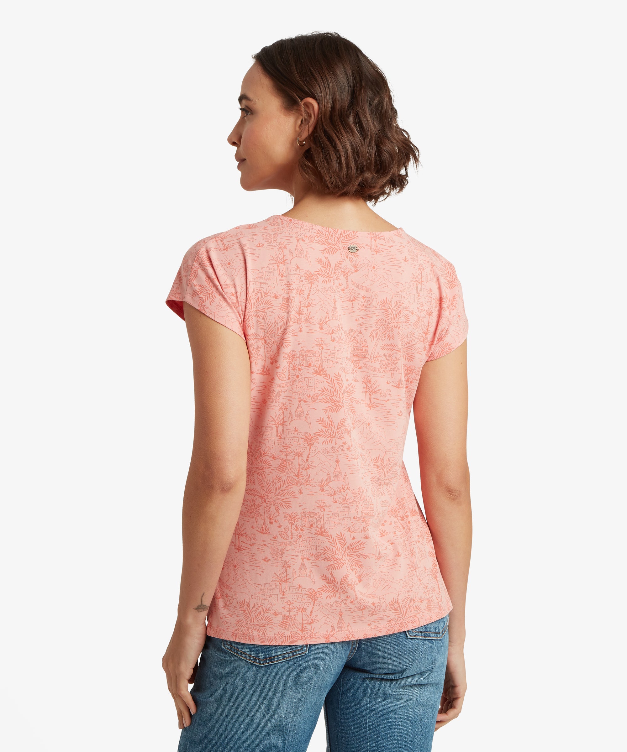 Rear view of a pale pink printed T‑shirt showing fine scenic Nepalese linework across the back, paired with blue jeans.