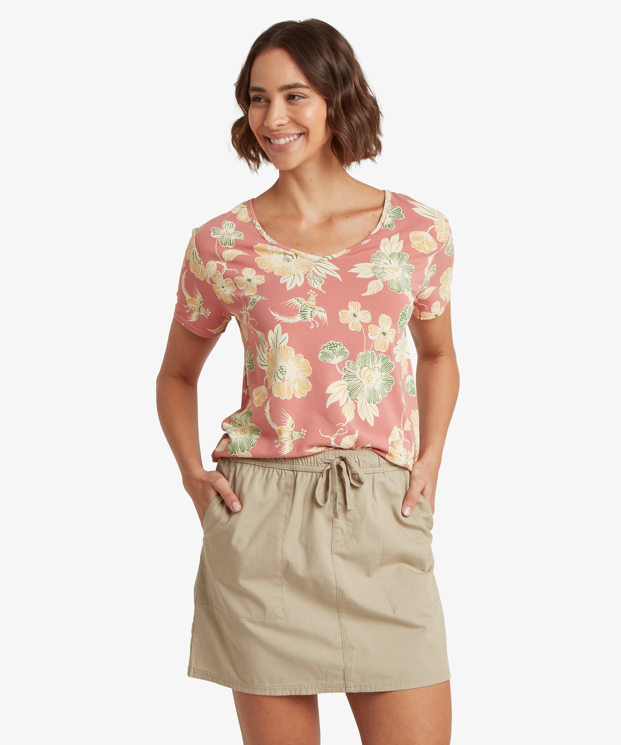 A floral V‑neck pink T‑shirt with soft yellow and green flowers paired with a beige drawstring skirt. The shirt has short sleeves and a comfortable draped fit.