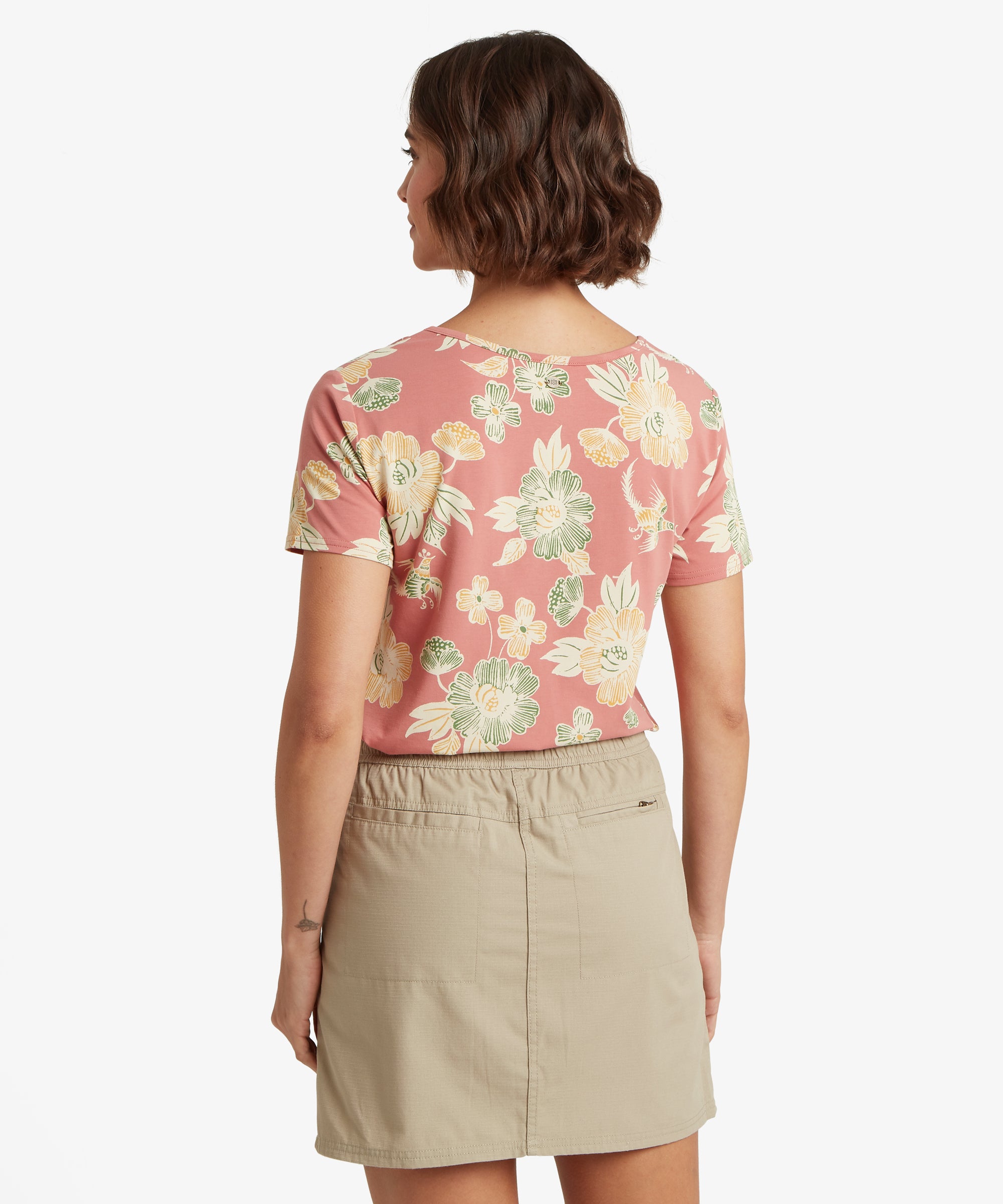 Rear view of a pink floral V‑neck tee worn with a beige drawstring skirt, showing the gathered waistband at the back.