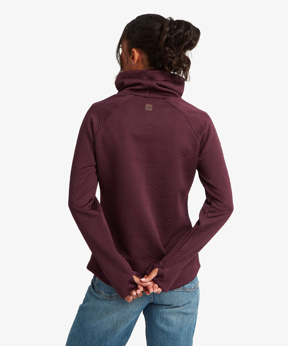 A woman viewed from the back wearing a textured, deep plum-purple long-sleeve top with a high folded collar.