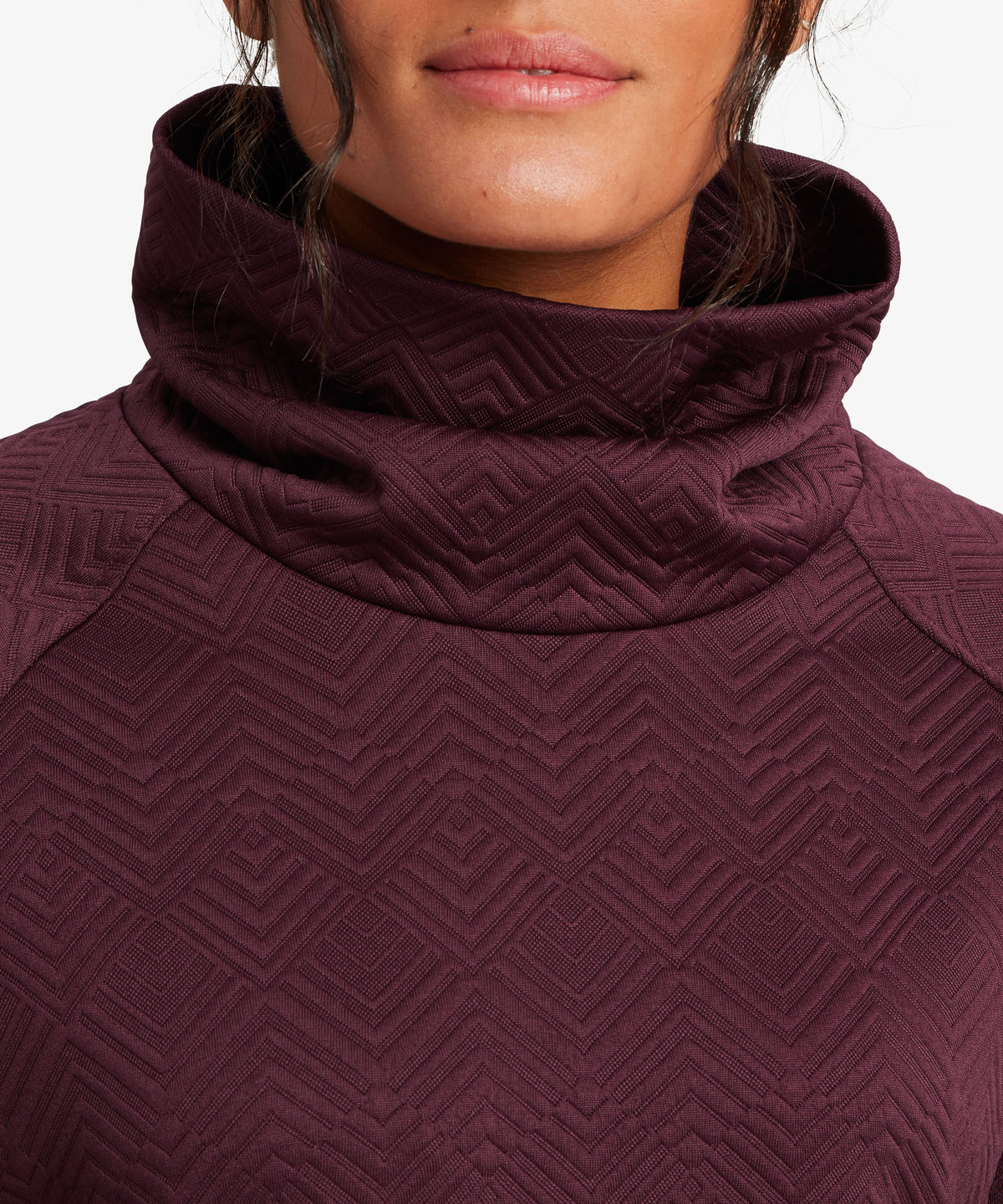 Close-up of a woman wearing a textured, deep burgundy turtleneck top with a geometric chevron pattern.