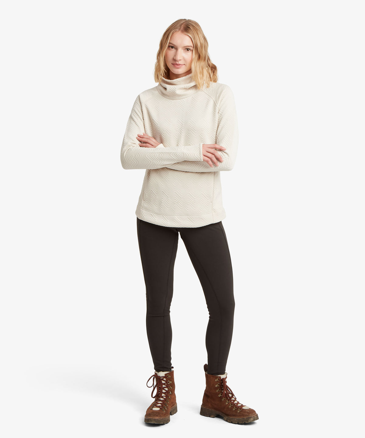 A full length picture of a woman modeling a cream-colored cowl-neck knit sweater.