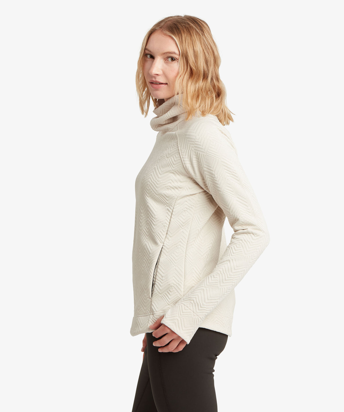 A woman modeling a cream-colored, textured knit cowl-neck sweater.
