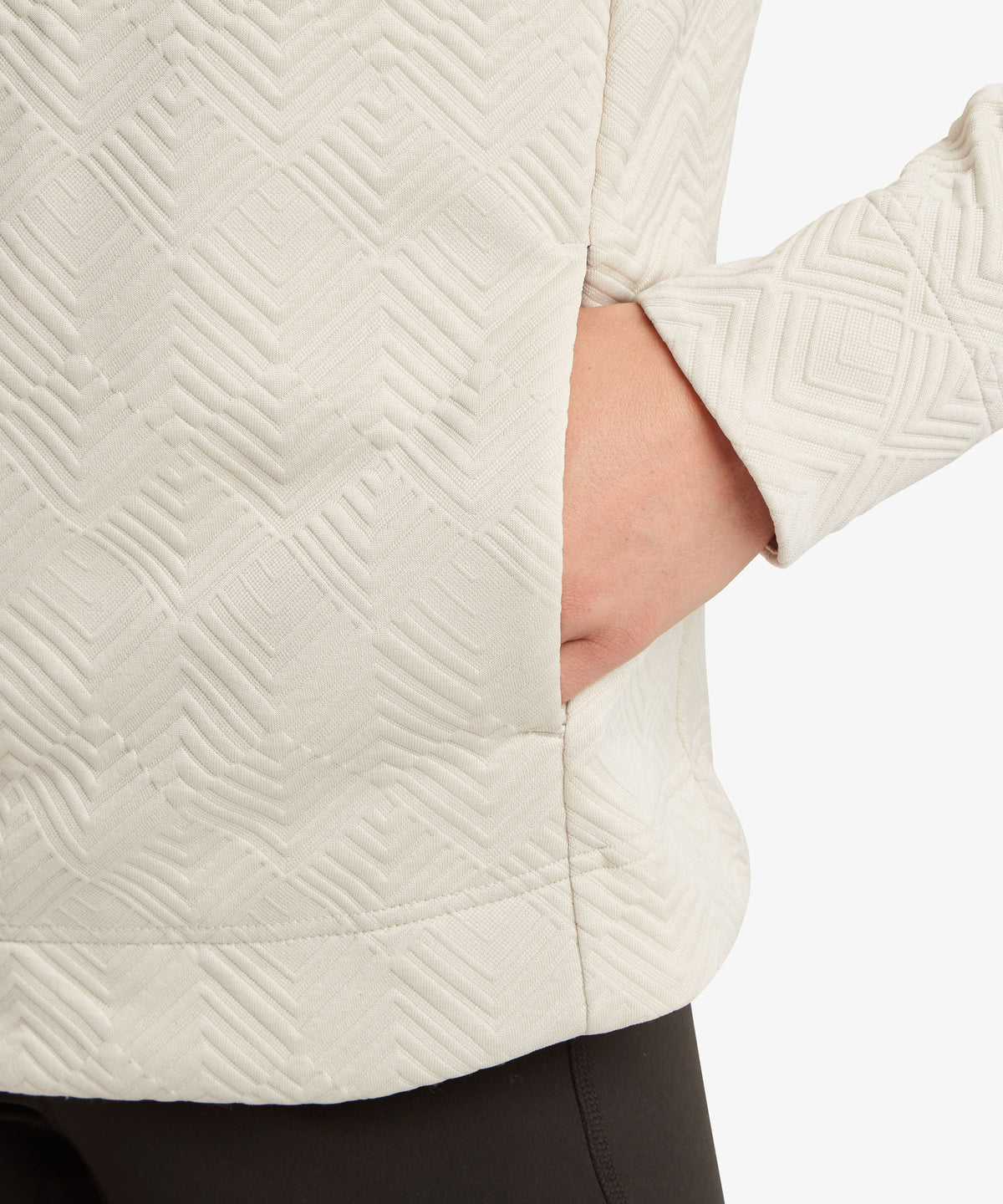 Close-up of a person wearing a cream-colored sweater with a geometric embossed pattern.