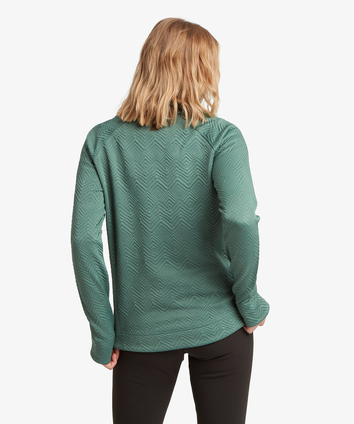 A woman viewed from the back wearing a sage green long-sleeve top with a textured chevron pattern.