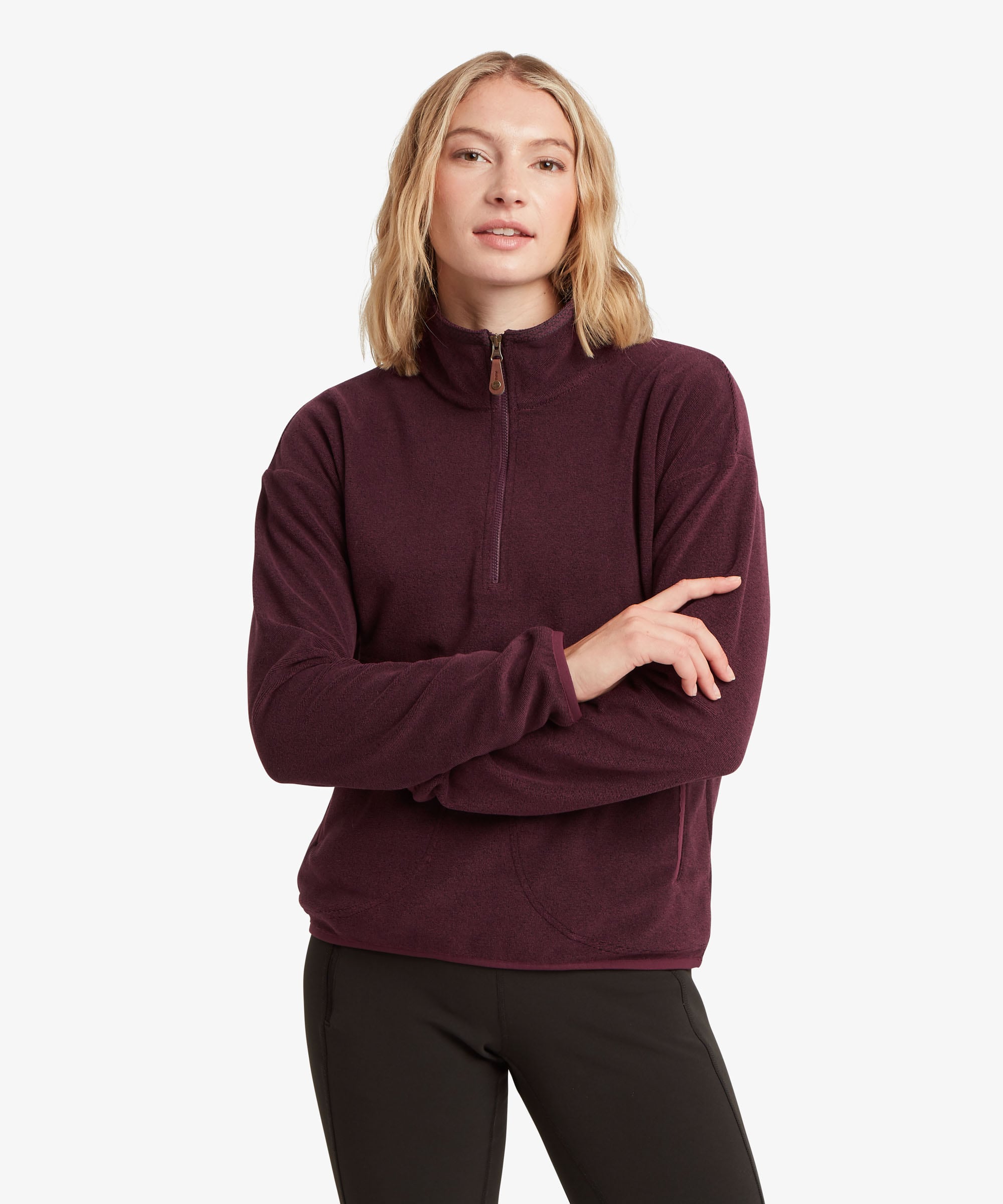 A female model, shown from the front, wearing the Sherpa Adventure Gear women's Rolpa 1/2 Zip in deep purple. The fleece features a high stand collar, half-zip front, long sleeves and a comfortable fit through the body. The model wears it with black trousers, clearly showing the rich purple colour and overall silhouette.