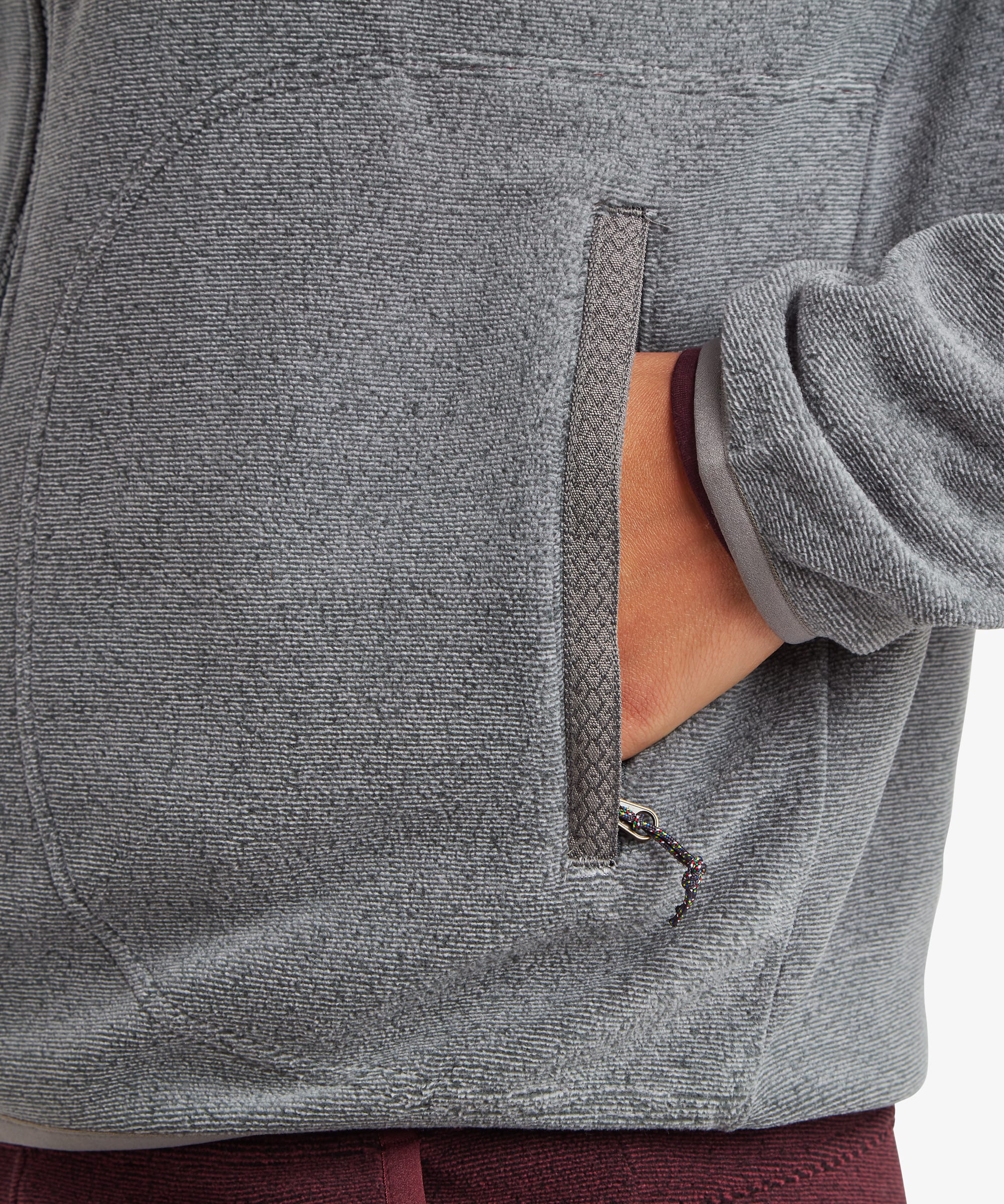 Close-up detail of the Sherpa Rolpa Full-Zip Fleece Jacket in grey showing the zippered hand pocket and textured fleece fabric.
