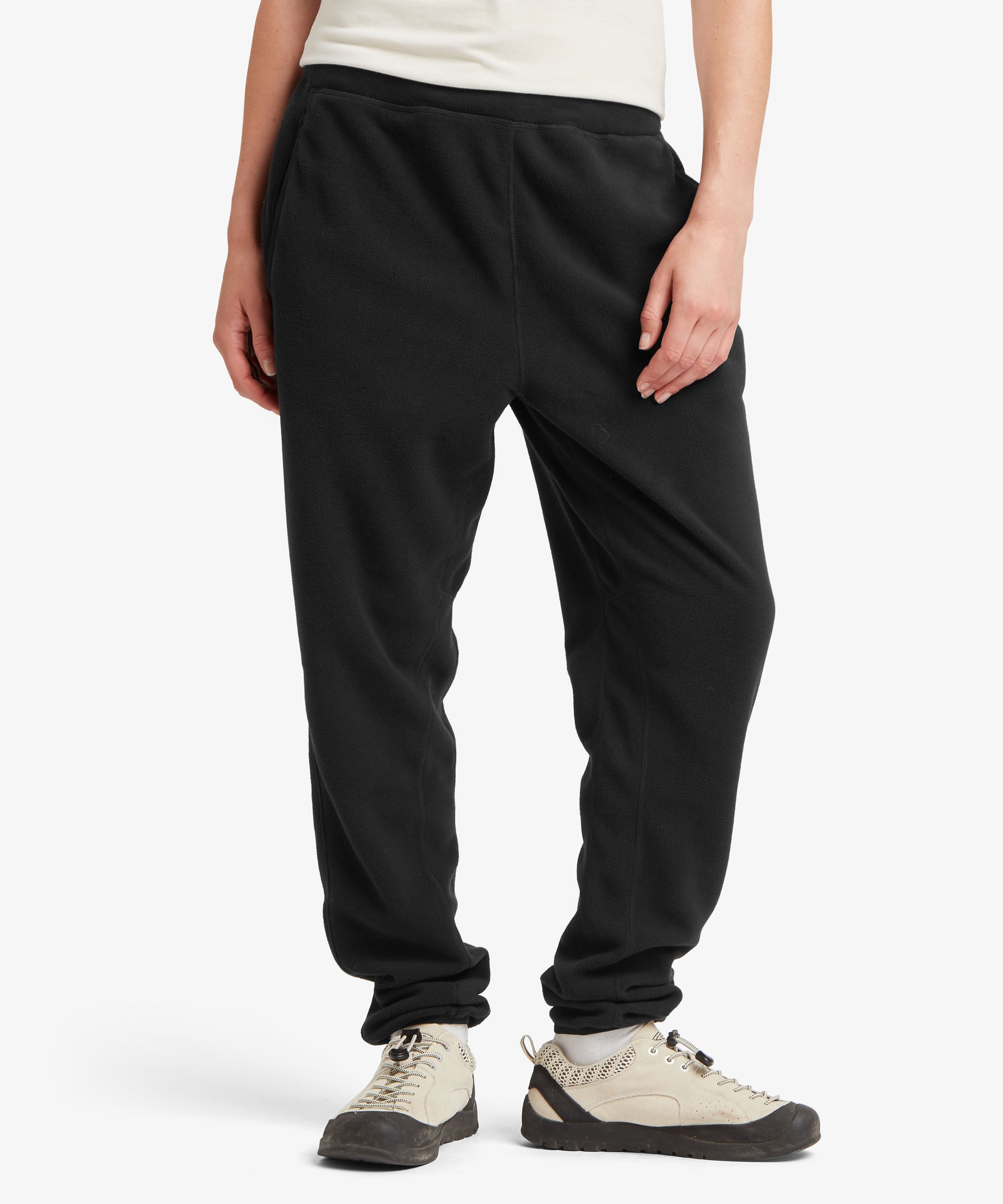 A female model wearing the Sherpa Adventure Gear black Rolpa Jogger trousers, shown from the waist down in a studio setting. The joggers have a relaxed tapered fit, elasticated ankle cuffs and a side hand pocket, with the soft fleece fabric clearly visible.