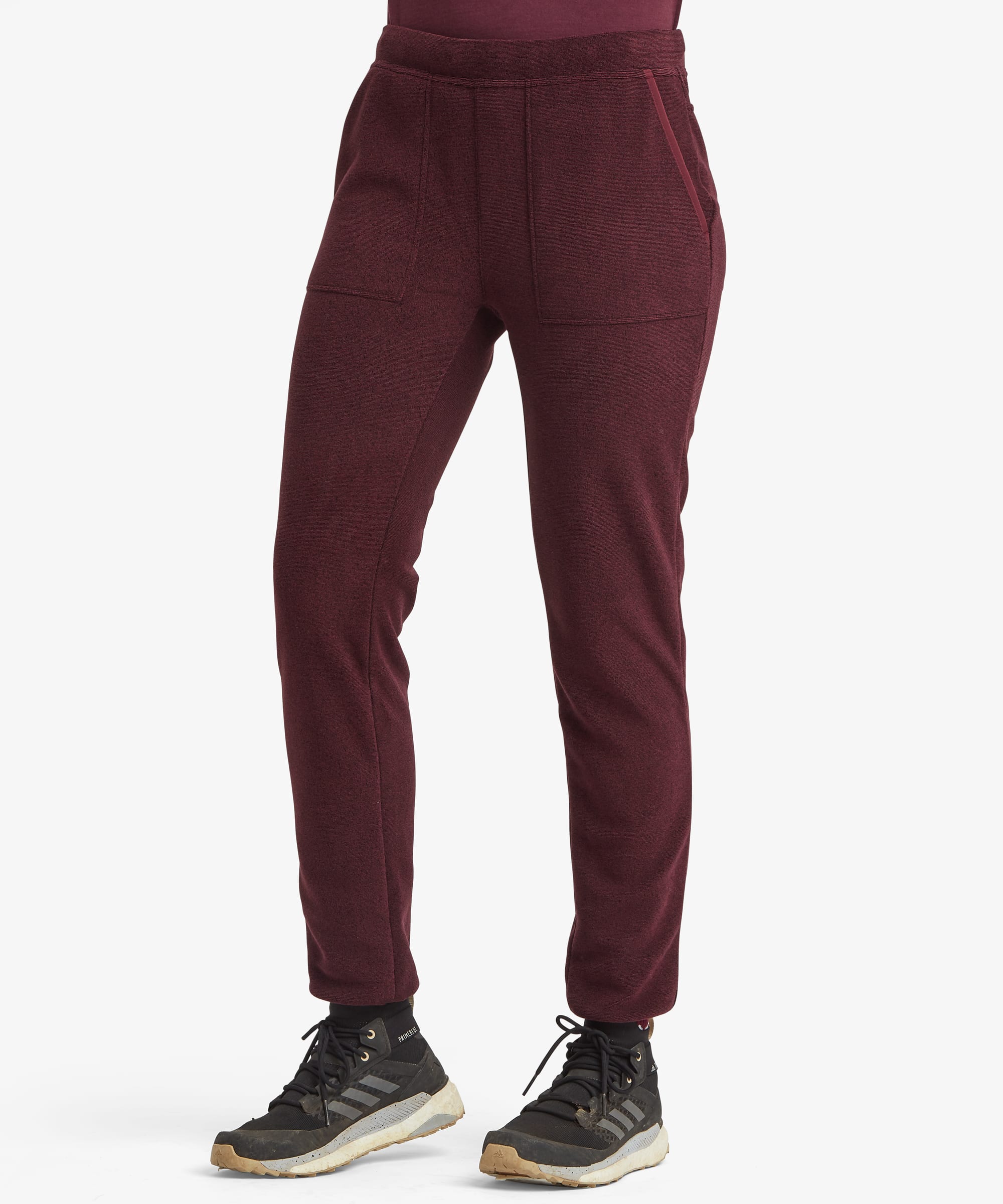 Front view of a woman wearing the Sherpa Rolpa Jogger in burgundy red, styled with a grey fleece jacket. The joggers feature a tapered leg, elasticated waistband and comfortable fleece construction.