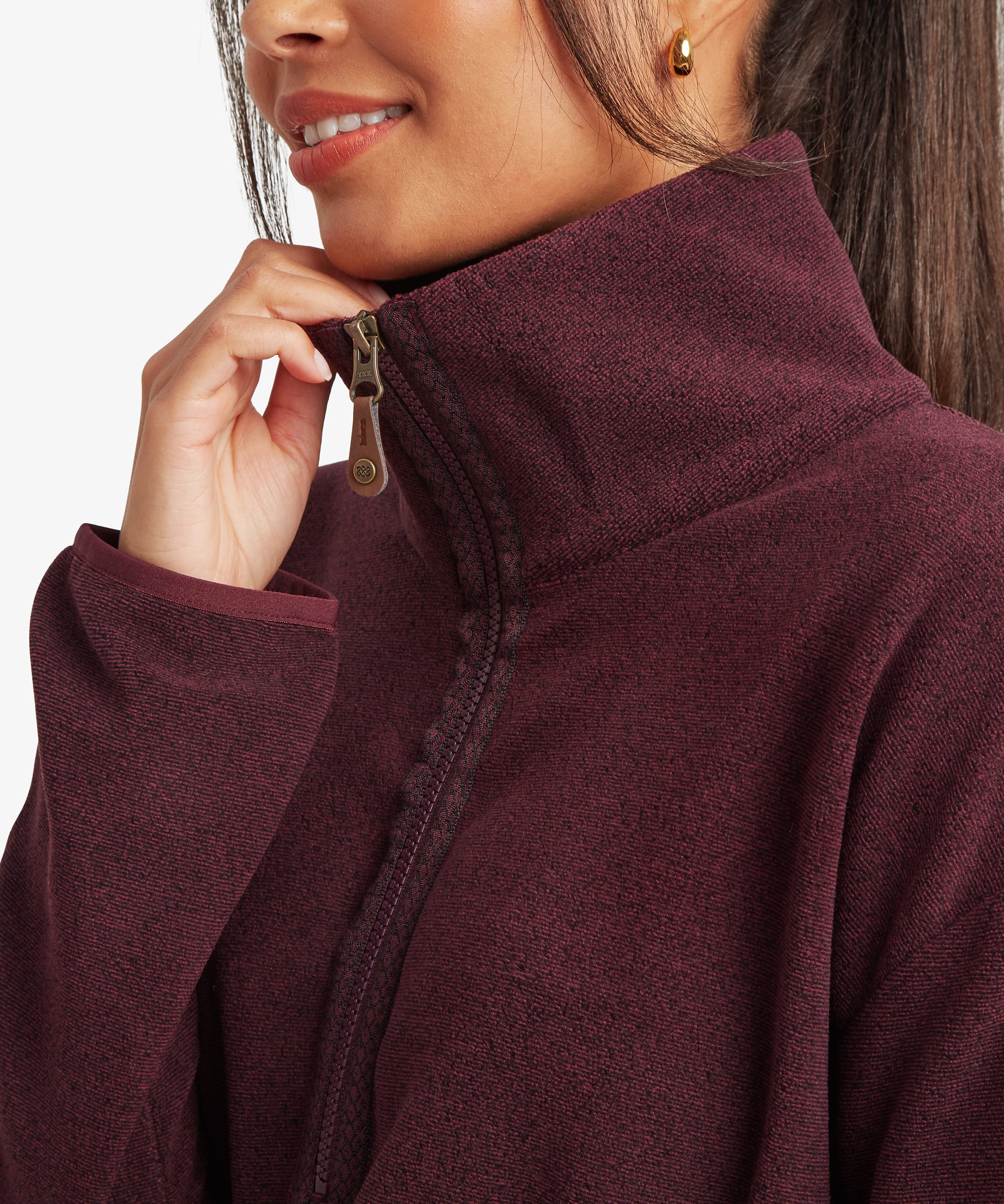 Close-up of the burgundy Sherpa Rolpa Pop Over fleece showing the high funnel neck, drawcord adjustment and soft textured fleece fabric. The model lightly touches the collar, highlighting the neckline construction.