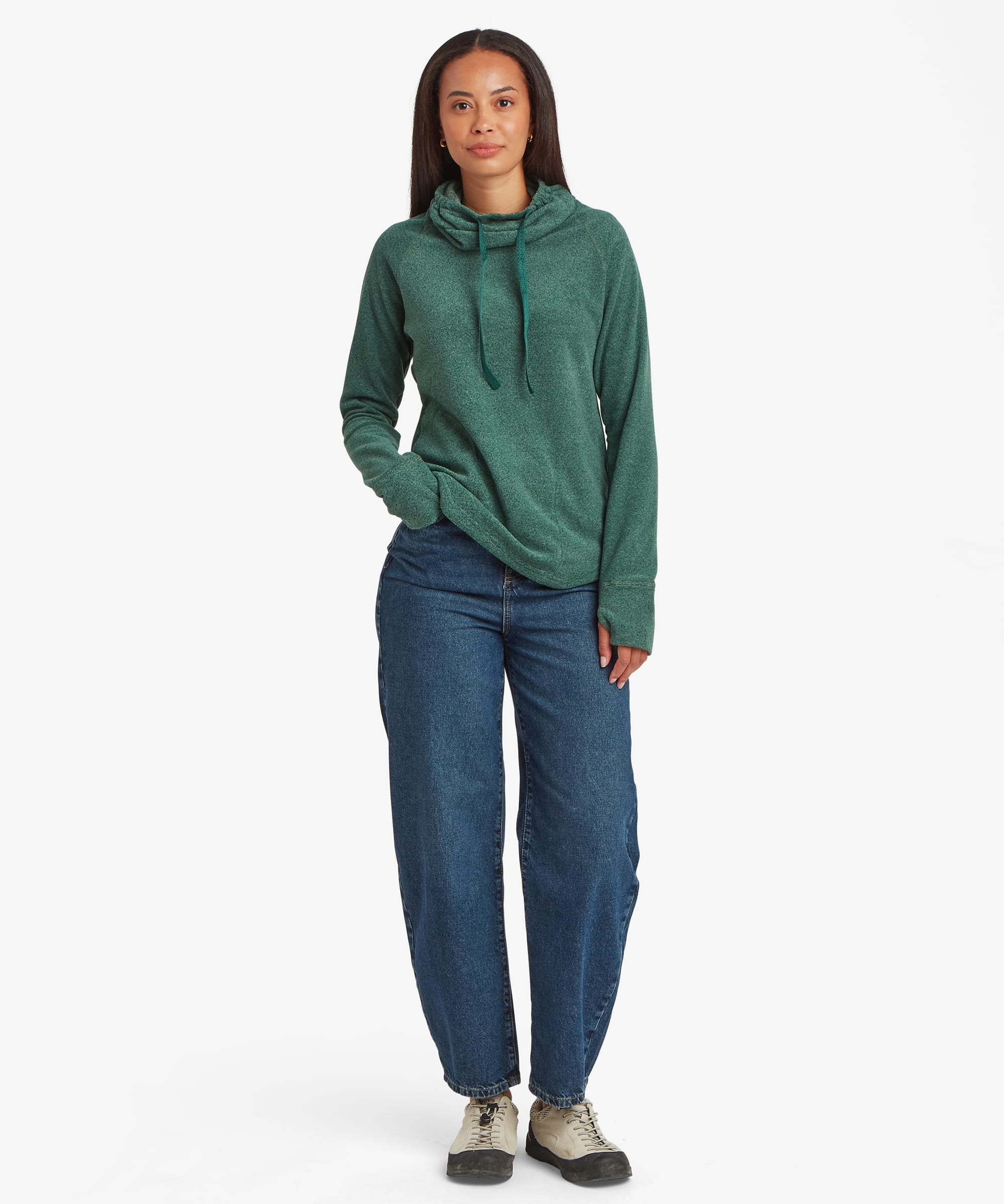 Full-length front view of a woman wearing a teal green Sherpa Rolpa Pullover paired with blue jeans and trainers. The image highlights the relaxed silhouette, high neckline and soft fleece texture.