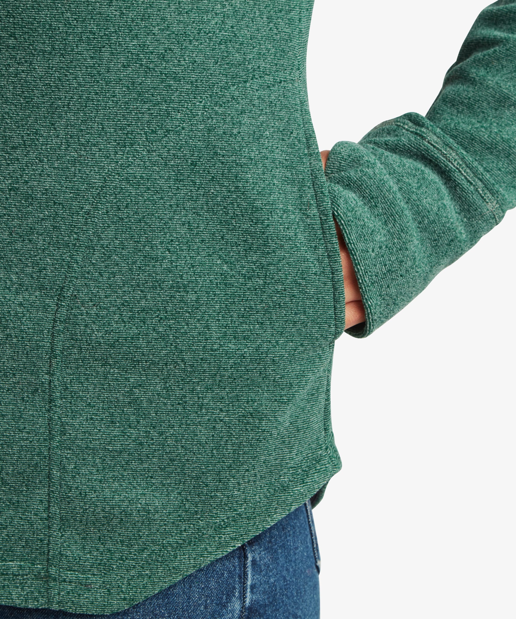 Close-up detail of the teal green Sherpa Rolpa Pullover showing the side seam pocket with the model's hand inserted. The image highlights the fleece texture and pocket construction.