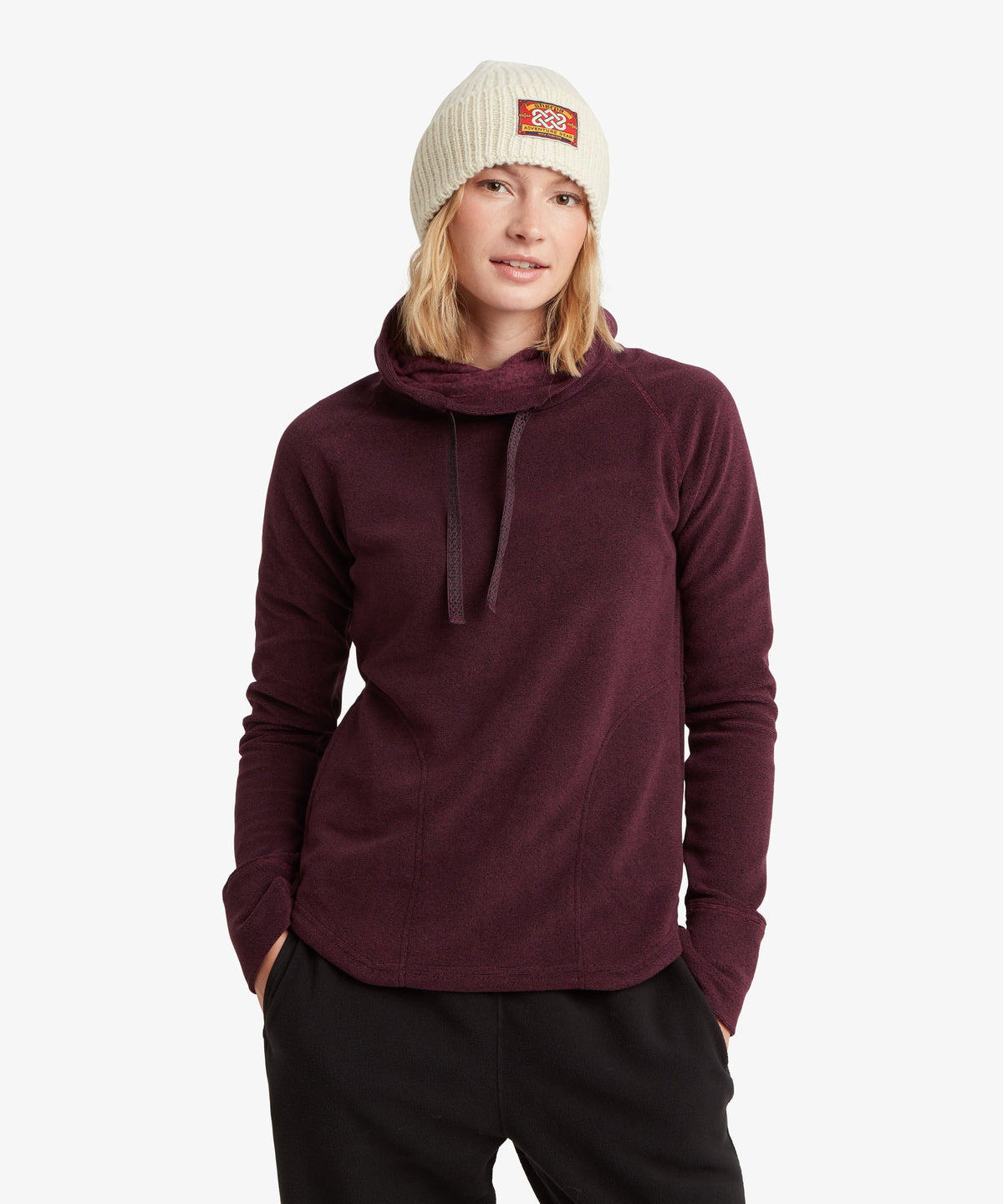 Front view of a woman wearing a deep plum fleece cowl-neck pullover and a cream knit beanie