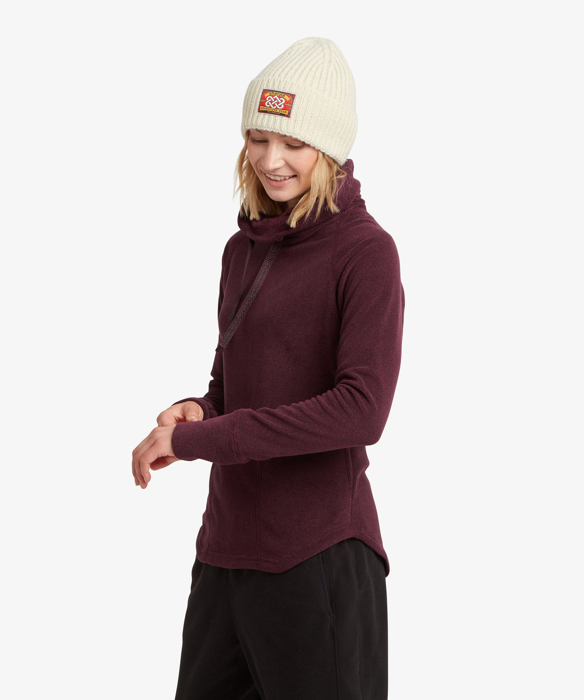 Three-quarter front view of a woman in a purple cowl-neck fleece pullover, black pants.