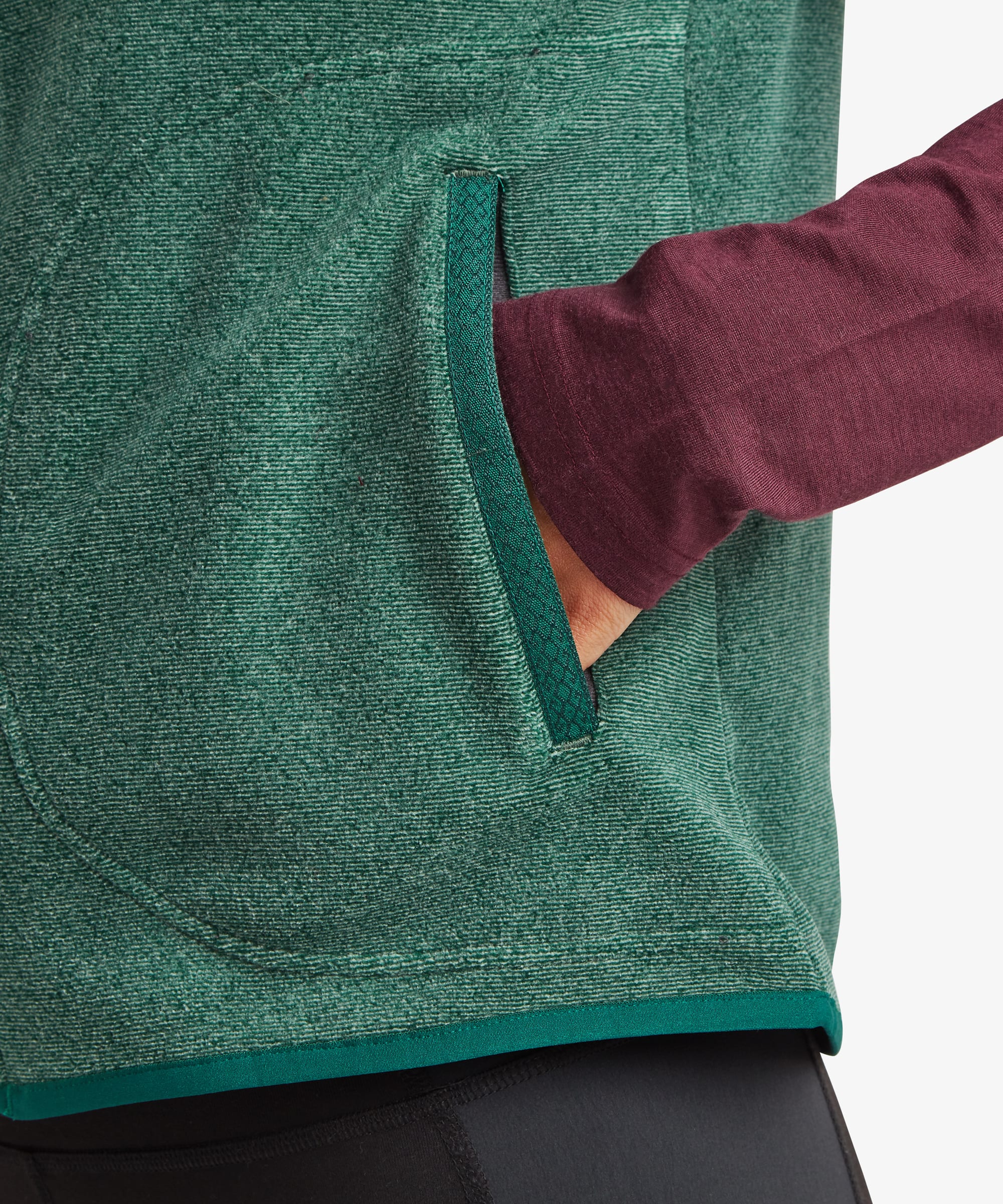 Detailed close-up of the deep green fleece vest highlighting the zippered hand pocket, textured fleece surface, and clean seam construction near the hem.