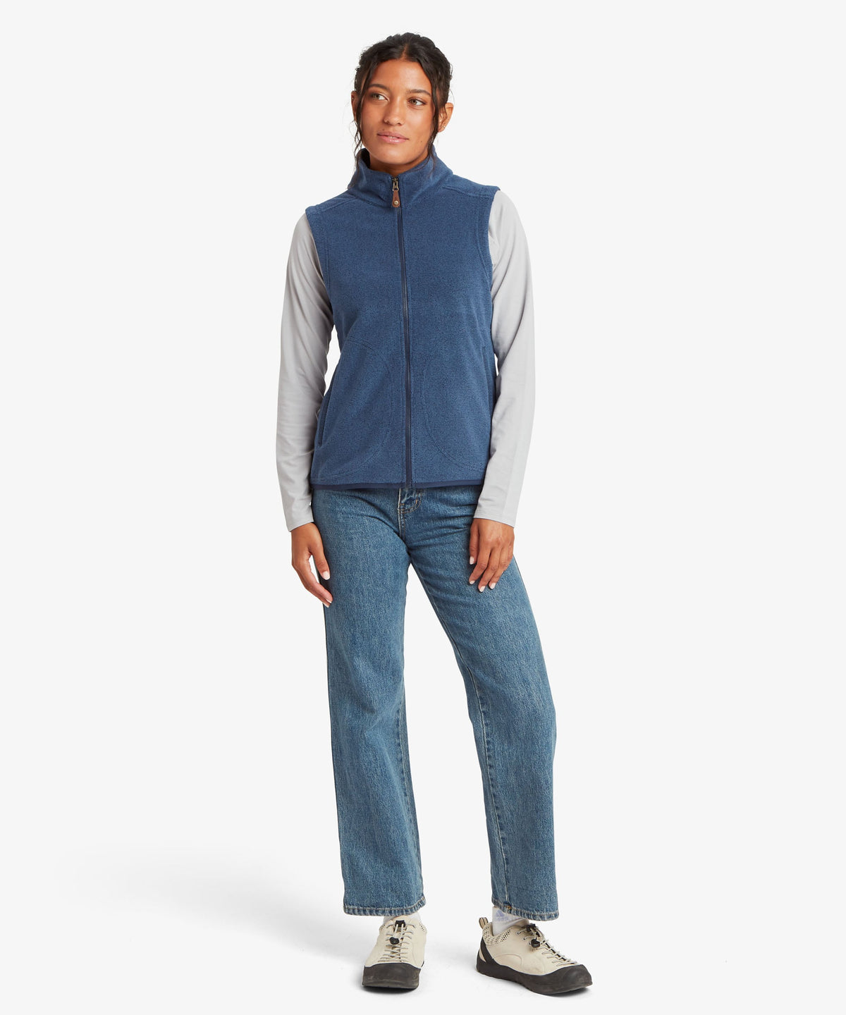 A woman modeling a sleeveless blue zip-front vest over light gray long sleeves.