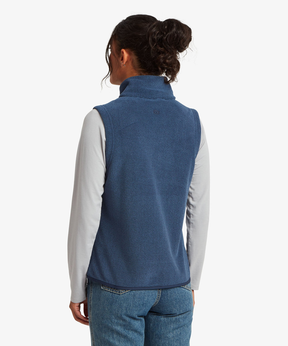 A woman shown from the back wearing a blue fleece vest over a light gray long-sleeve shirt.