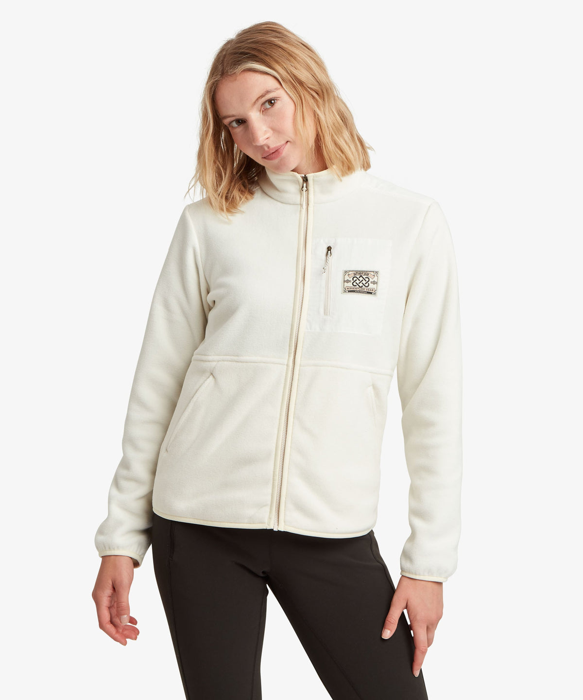 A female model wearing the Sherpa Adventure Gear white Sanu Full-Zip fleece with black trousers.
