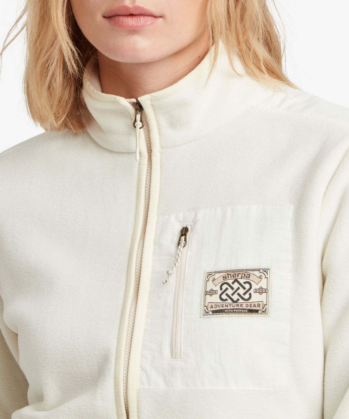 A female model wearing the Sherpa Adventure Gear white Sanu Full-Zip fleece, shown in close-up.