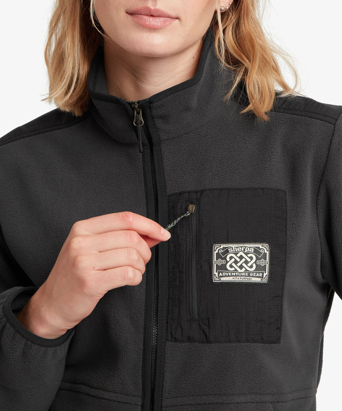 A female model wearing the Sherpa Adventure Gear black Sanu Full-Zip fleece, shown in close-up.