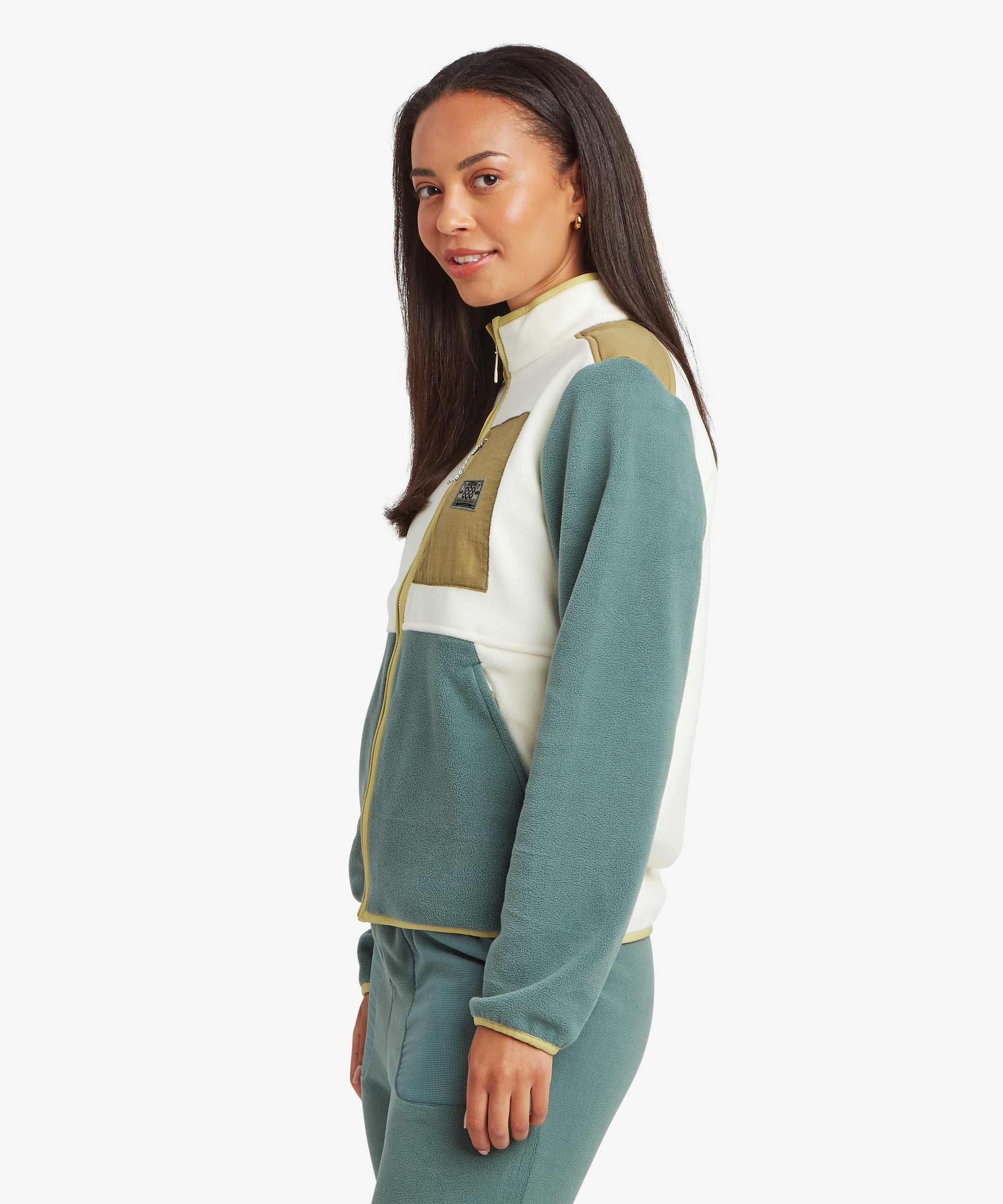 Side-profile studio view of a woman wearing a colour-block fleece jacket featuring green, cream, and tan panels. The image showcases the jacket's shape through the body and sleeves.