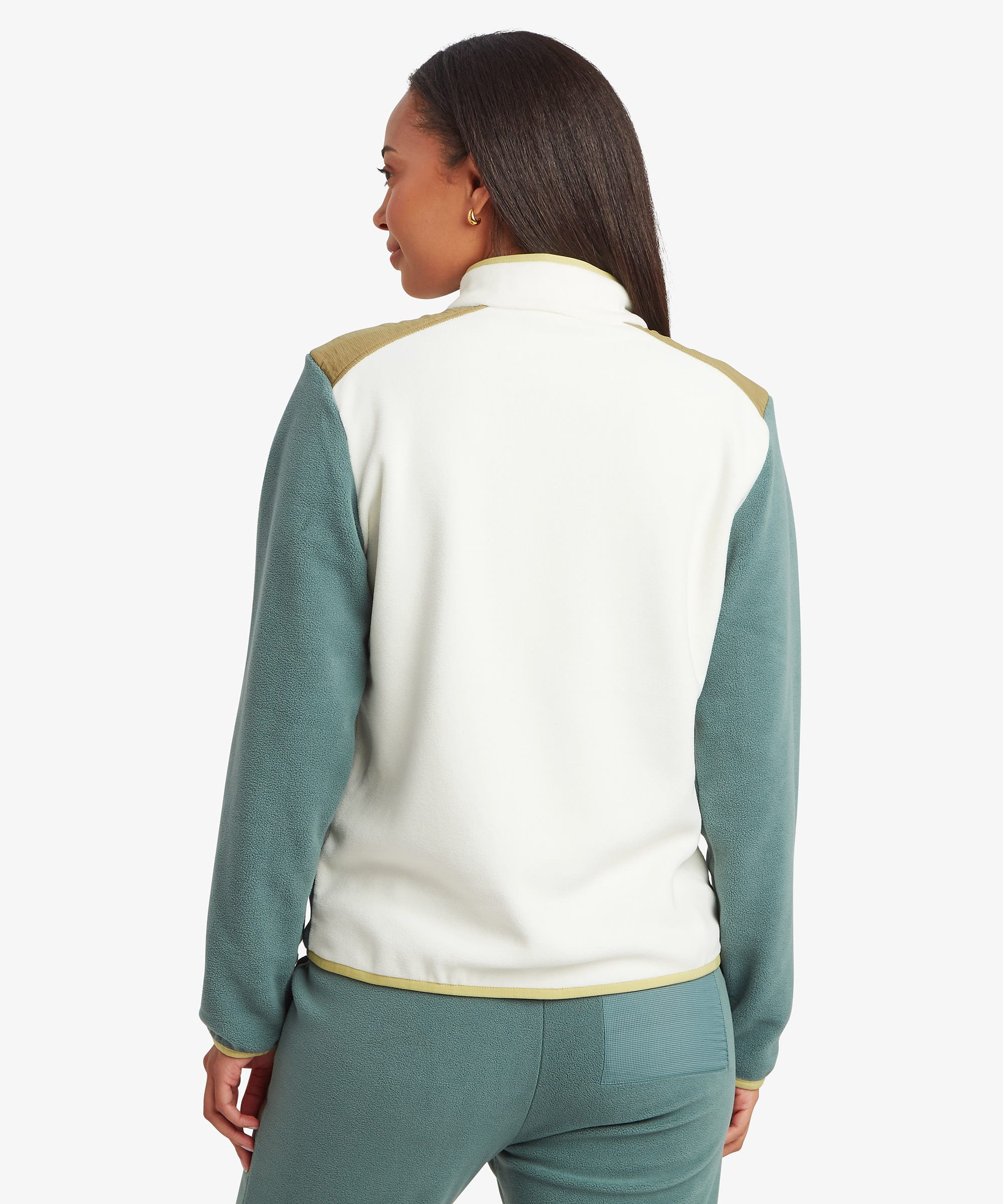 Rear studio view of a woman wearing a cream and green colour-block fleece jacket paired with matching green trousers. The image highlights the back panel design and relaxed fit.