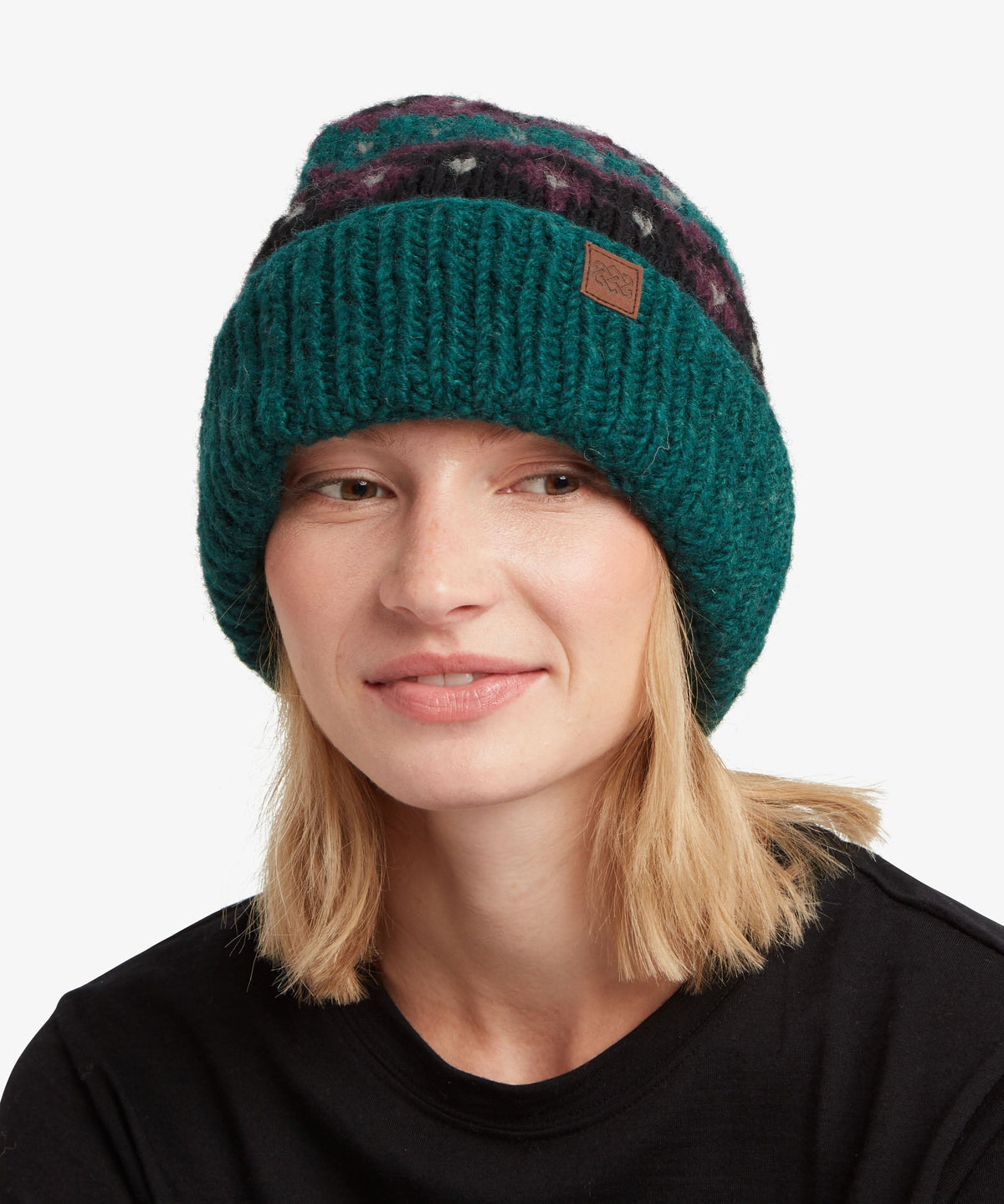A woman wearing a dark teal green knit beanie with a brown leather patch logo on the side.