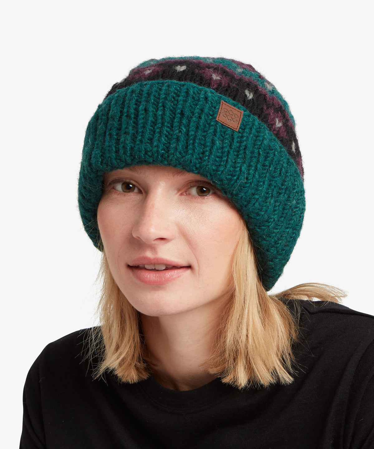 A woman wearing a dark teal knit beanie with a brown patch logo.