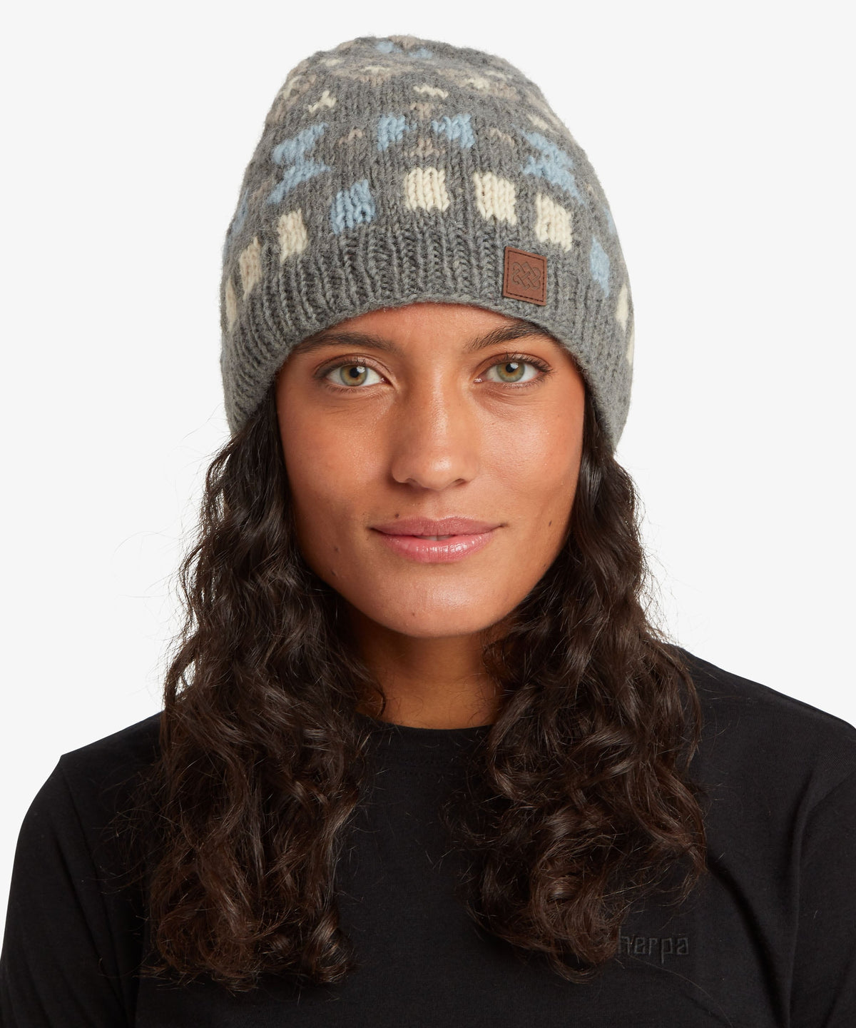 A woman with long dark curly hair wearing a gray knit beanie hat with a light blue.