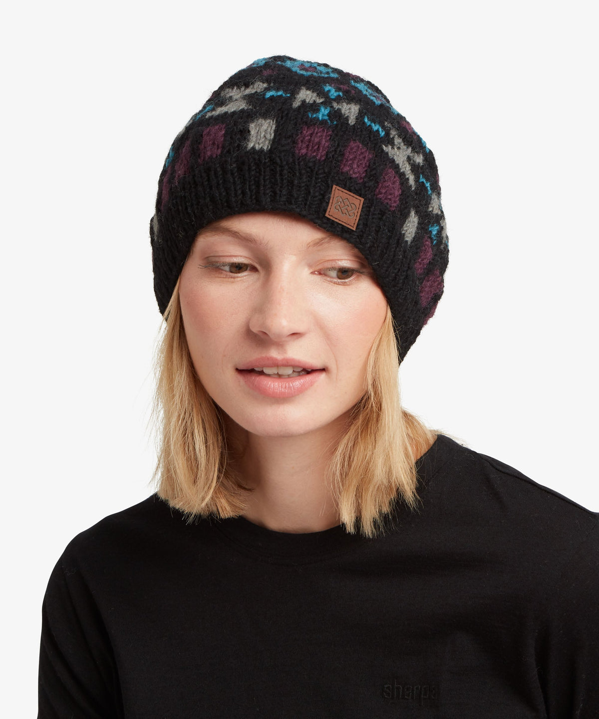 A woman wearing a black knit beanie with a colorful geometric pattern in blue, purple.