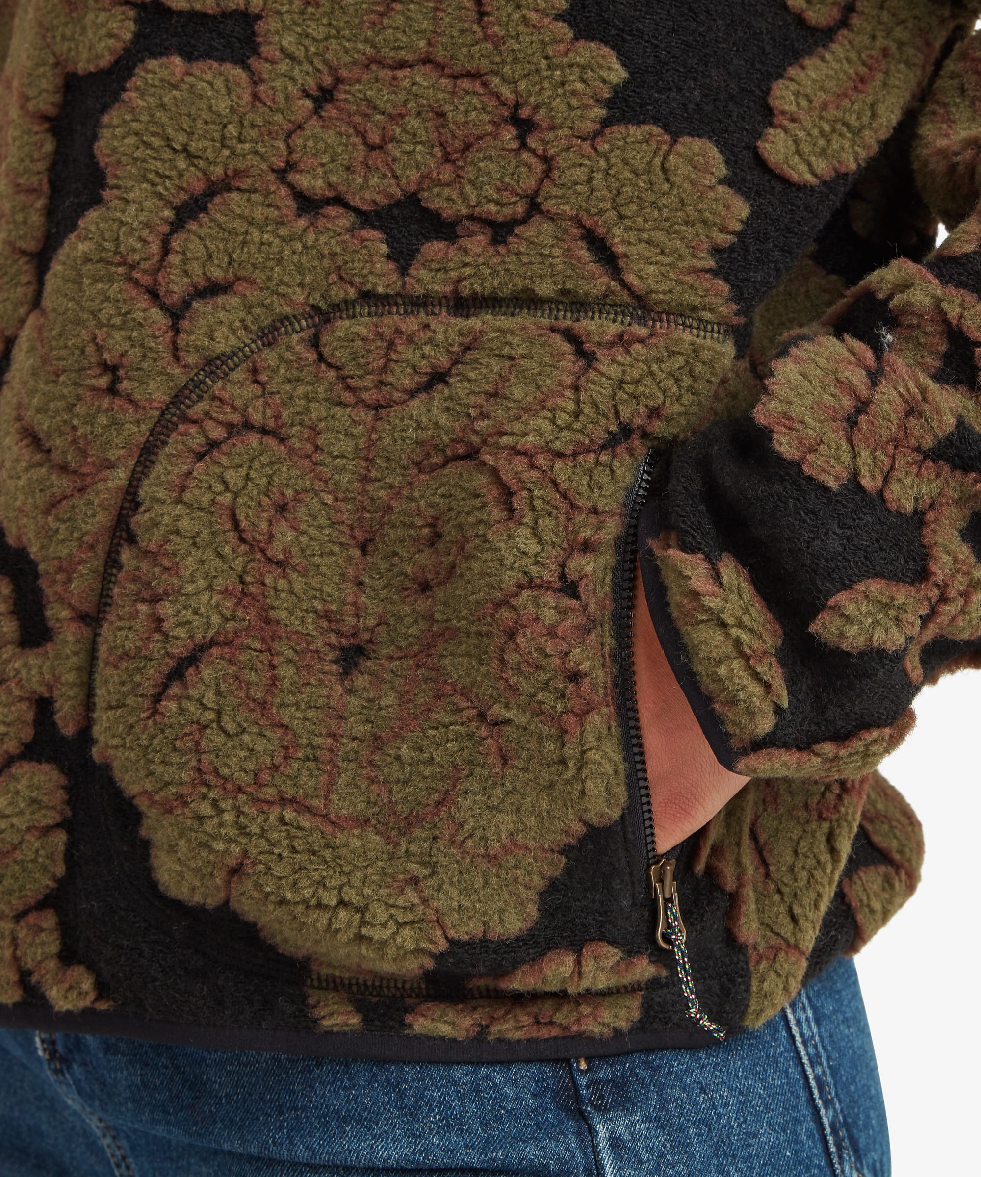 Detailed close-up of the dark green floral fleece pullover showing the quarter-zip opening, oversized botanical pattern, and soft textured fabric near the side seam and hem.