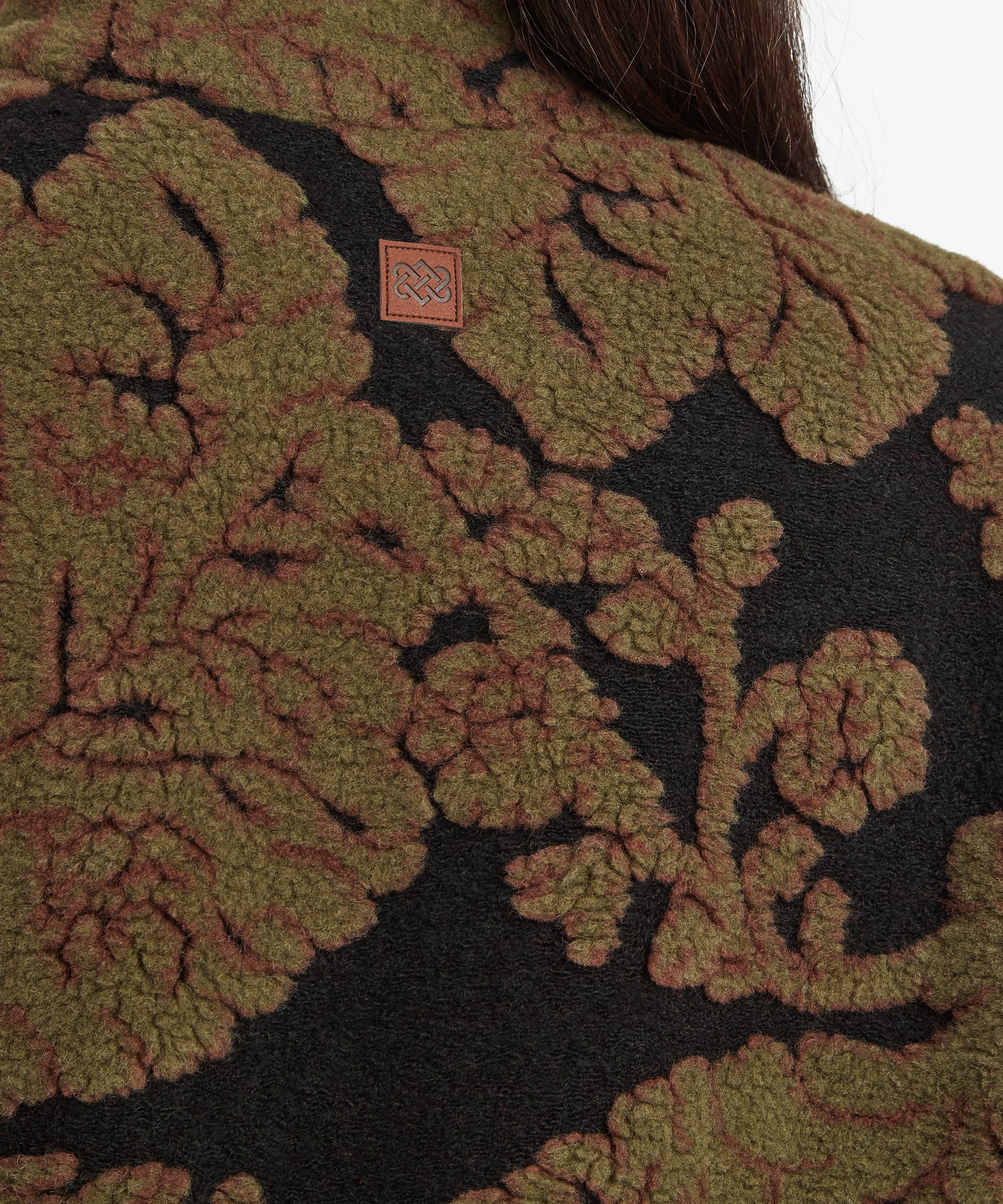 Fabric detail image highlighting the large floral jacquard pattern woven into the dark green fleece. The close crop focuses on the texture, colour contrast, and intricate botanical design.